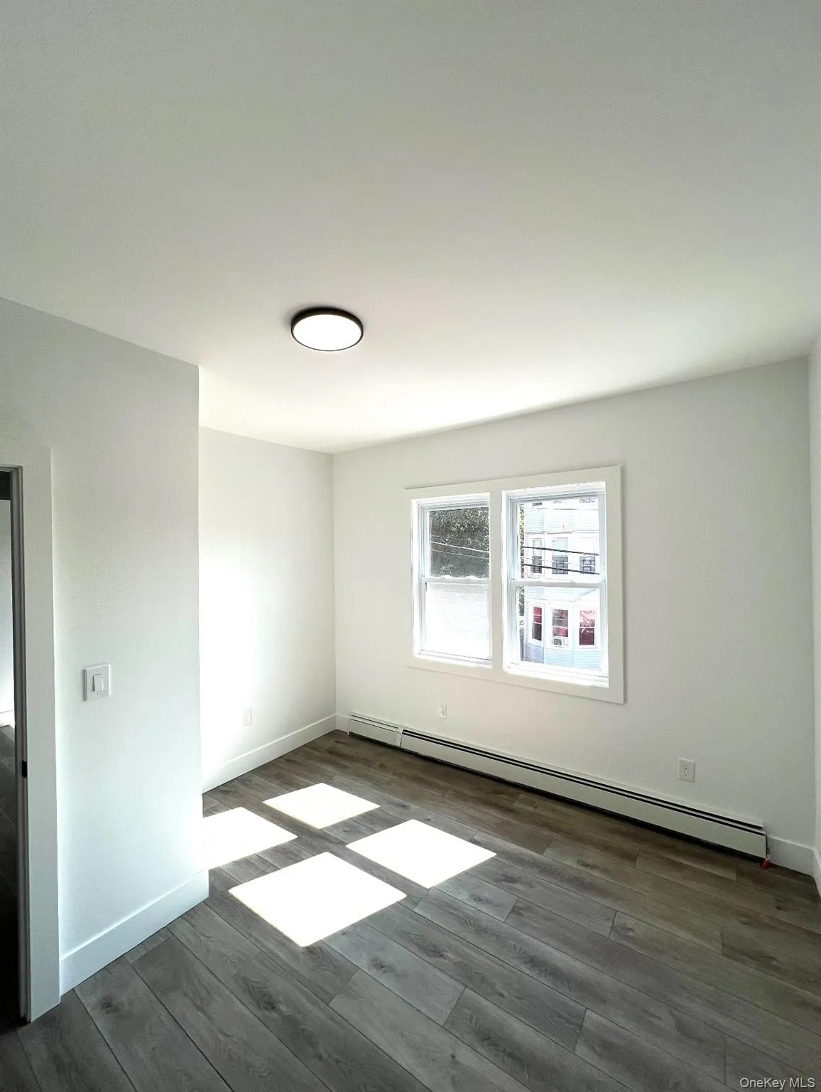 Unfurnished room with a baseboard heating unit and dark wood-style flooring Unfurnished room with a baseboard heating unit and dark wood-style flooring