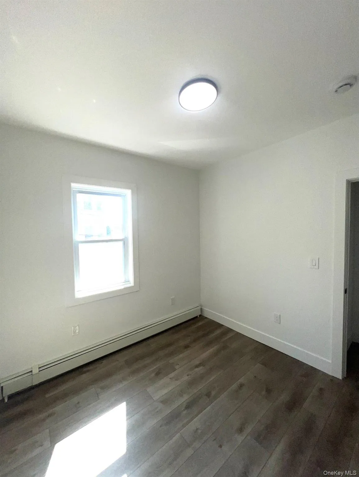 Empty room with a baseboard heating unit and dark wood-style floors Empty room with a baseboard heating unit and dark wood-style floors
