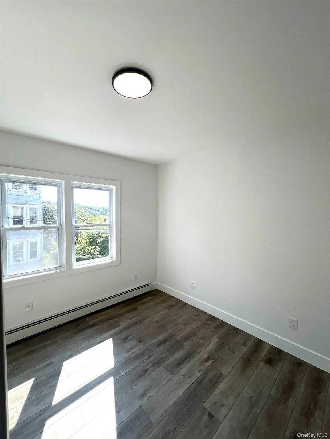 Spare room with a baseboard radiator and dark wood-style floors Spare room with a baseboard radiator and dark wood-style floors