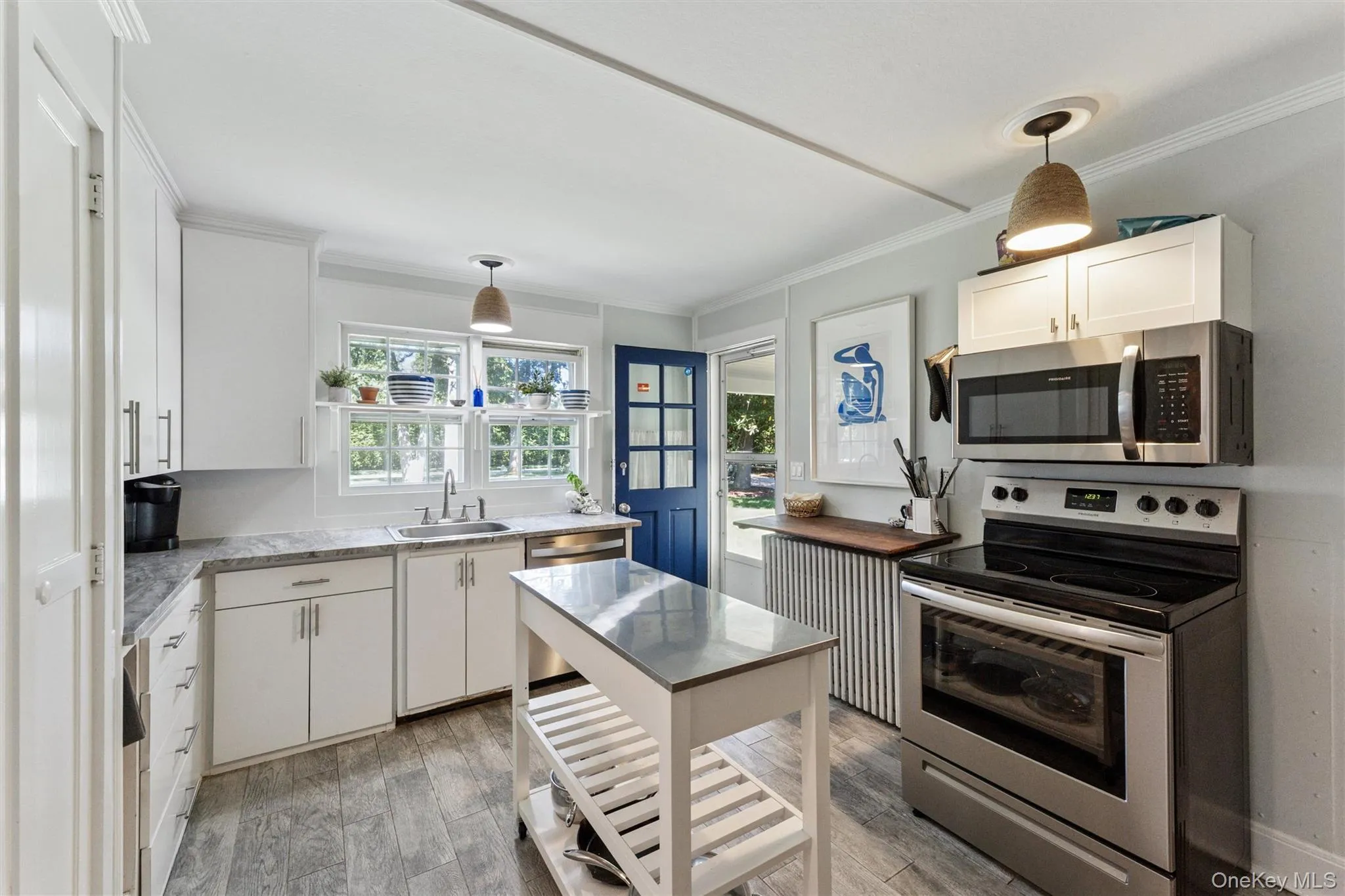 Kitchen featuring stainless steel appliances, crown molding, hanging light fixtures, white cabinetry, and light wood finished floors Kitchen featuring stainless steel appliances, crown molding, hanging light fixtures, white cabinetry, and light wood finished floors