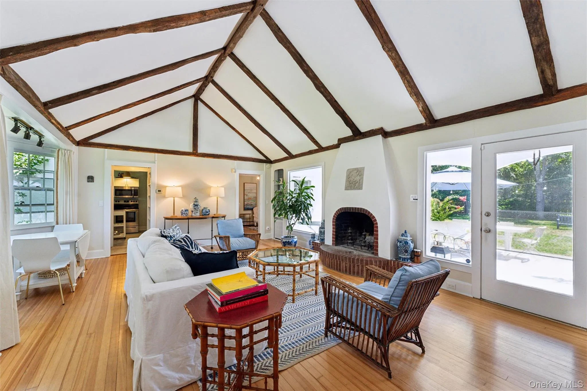 Living room with healthy amount of natural light, light wood-style floors, high vaulted ceiling, beam ceiling, and a brick fireplace Living room with healthy amount of natural light, light wood-style floors, high vaulted ceiling, beam ceiling, and a brick fireplace