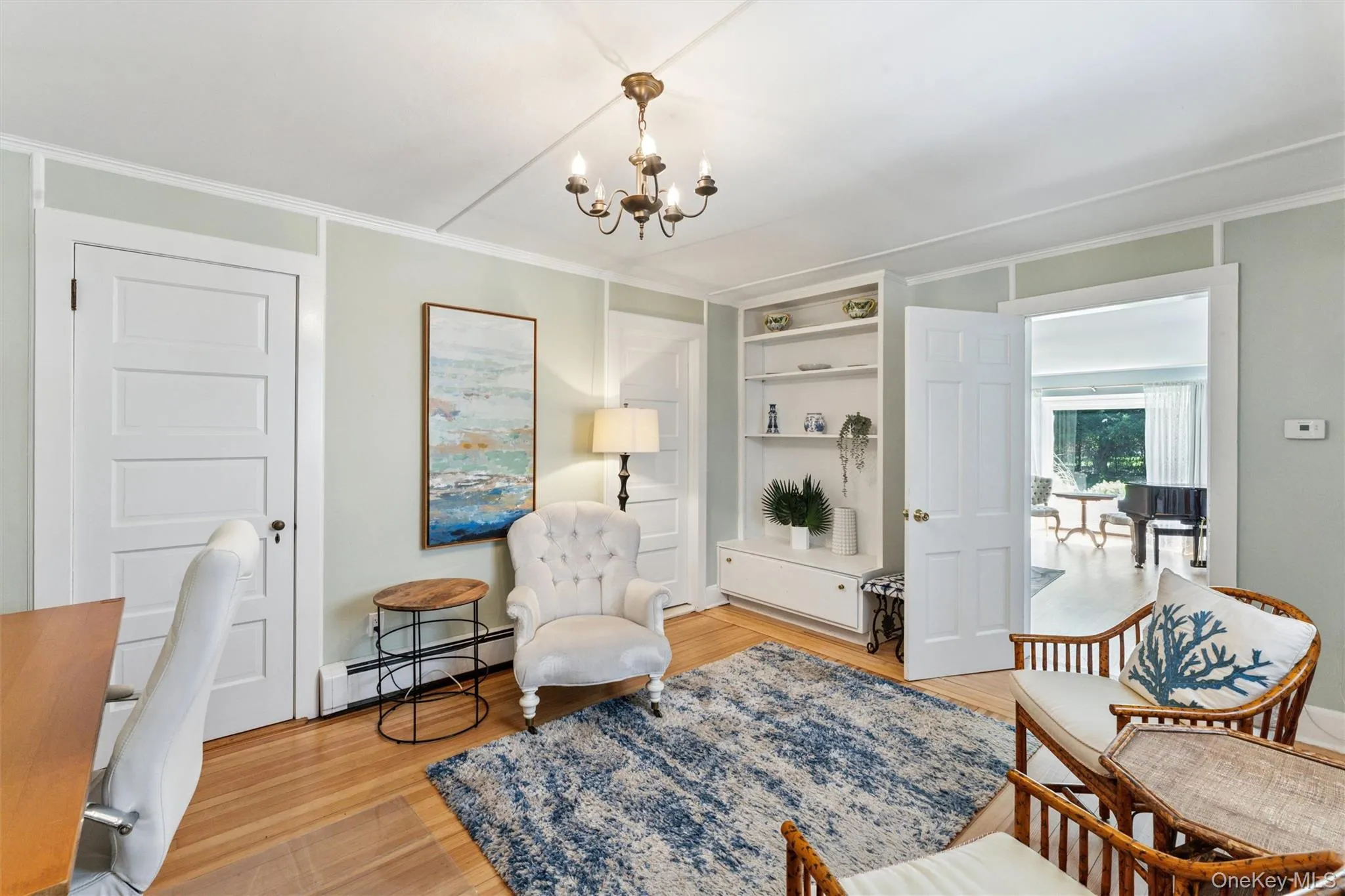 Sitting room with a baseboard radiator, light wood-style flooring, a chandelier, built in shelves, and crown molding Sitting room with a baseboard radiator, light wood-style flooring, a chandelier, built in shelves, and crown molding