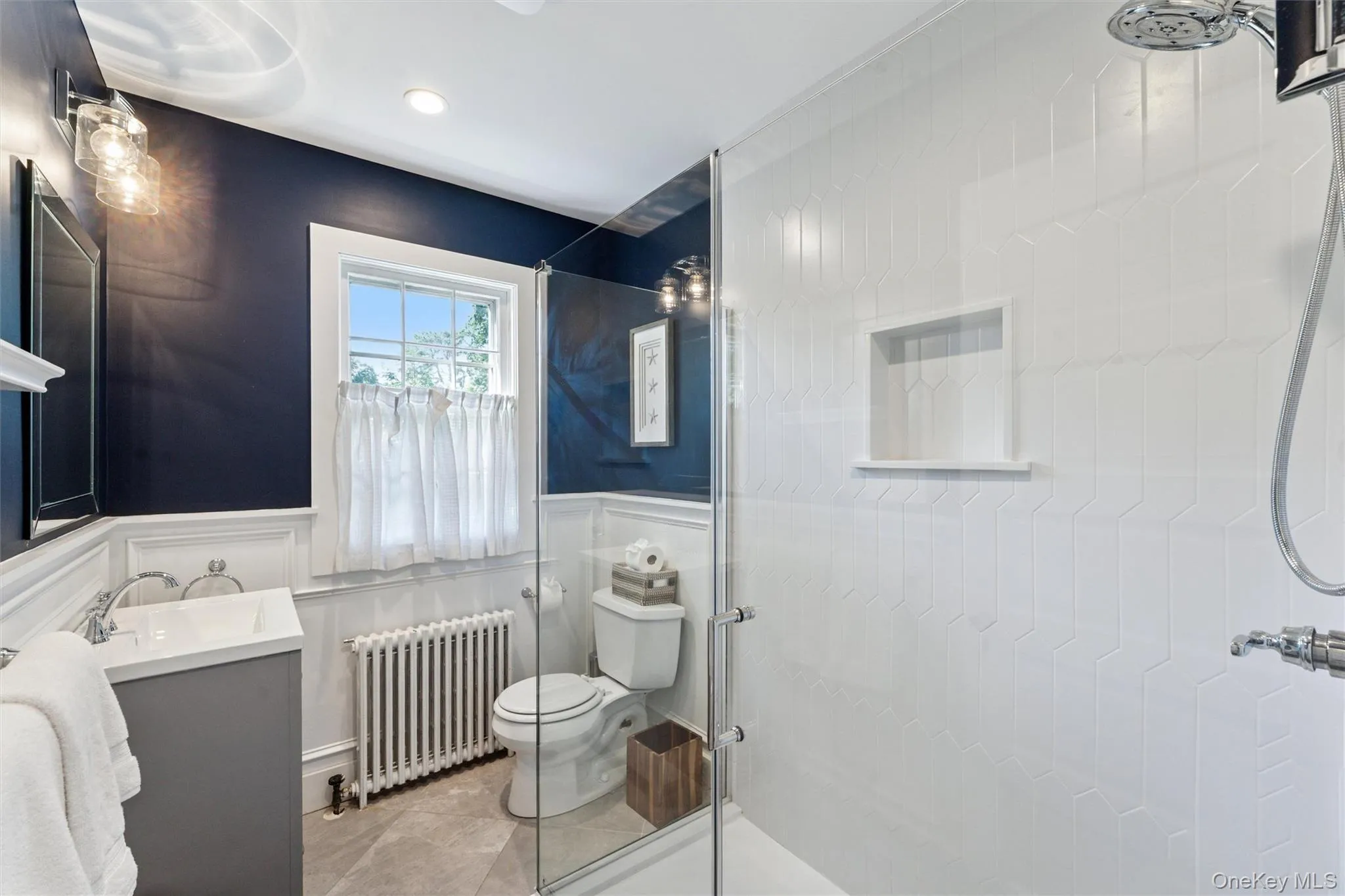 Bathroom featuring a shower stall, vanity, radiator heating unit, a wainscoted wall, and recessed lighting Bathroom featuring a shower stall, vanity, radiator heating unit, a wainscoted wall, and recessed lighting