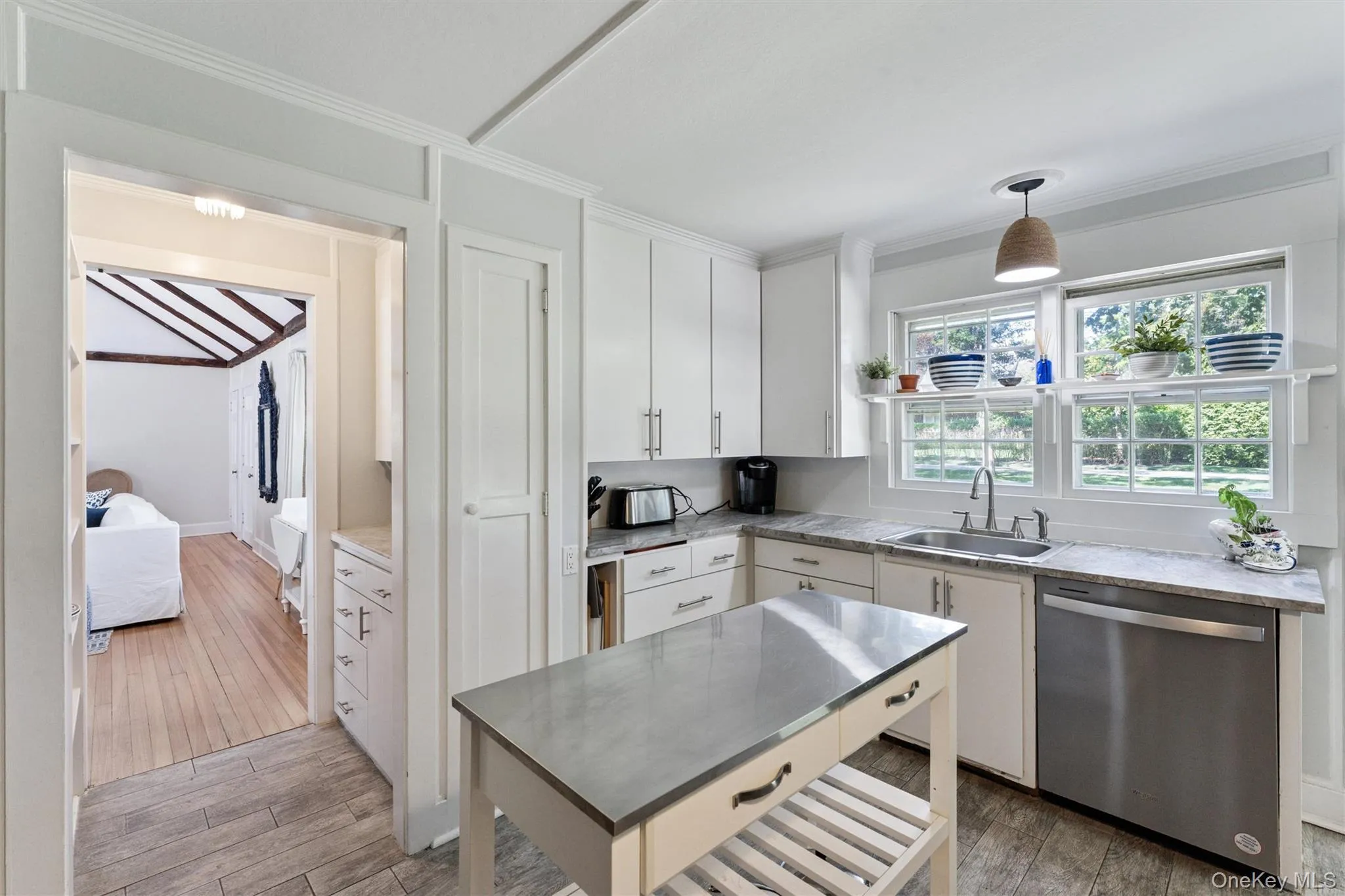 Kitchen featuring dishwasher, light wood finished floors, decorative light fixtures, white cabinetry, and ornamental molding Kitchen featuring dishwasher, light wood finished floors, decorative light fixtures, white cabinetry, and ornamental molding