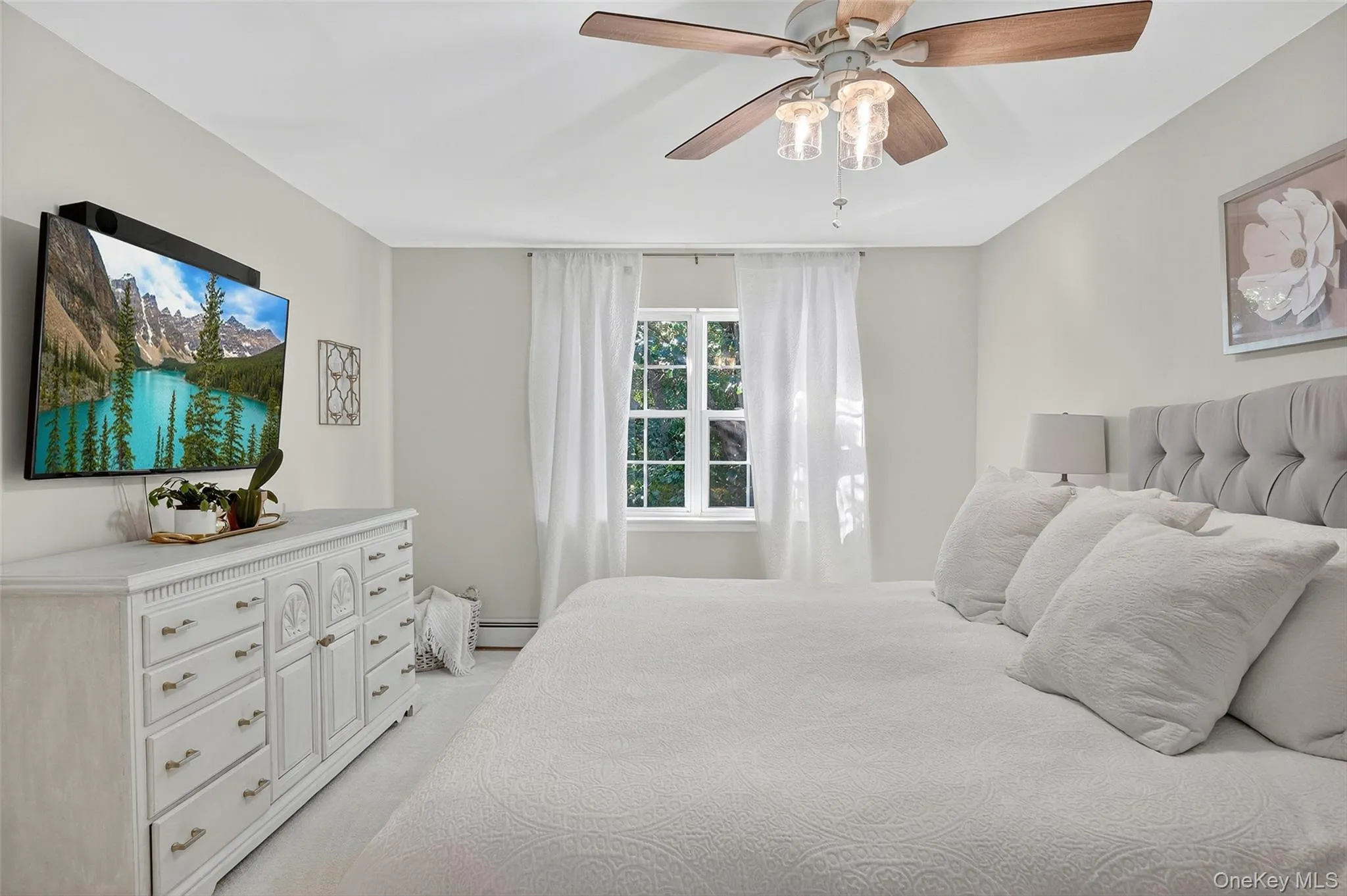 Bedroom featuring light carpet, ceiling fan, and a baseboard radiator Bedroom featuring light carpet, ceiling fan, and a baseboard radiator