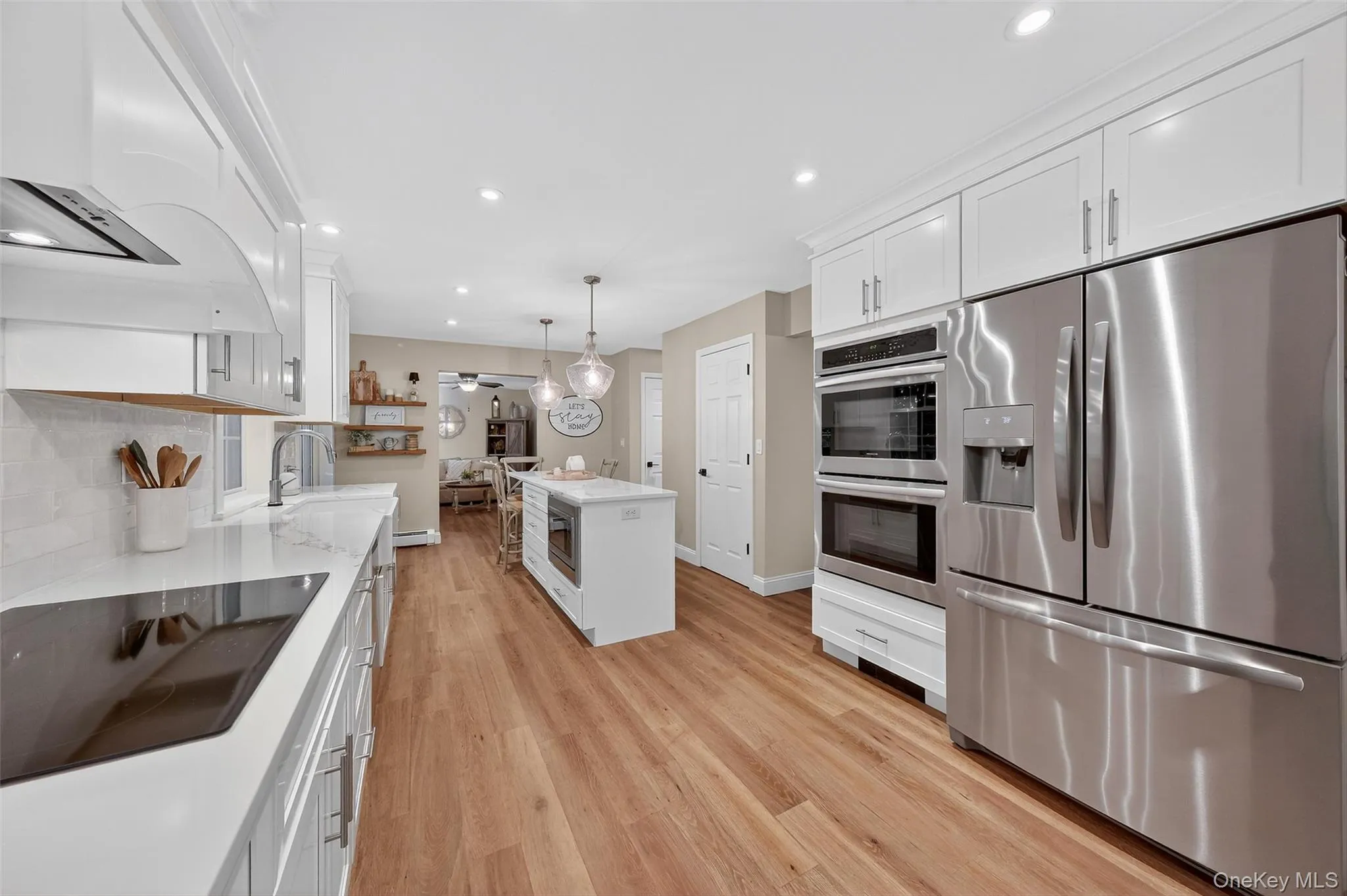 Kitchen featuring stainless steel appliances, white cabinets, hanging light fixtures, recessed lighting, and light wood-type flooring Kitchen featuring stainless steel appliances, white cabinets, hanging light fixtures, recessed lighting, and light wood-type flooring