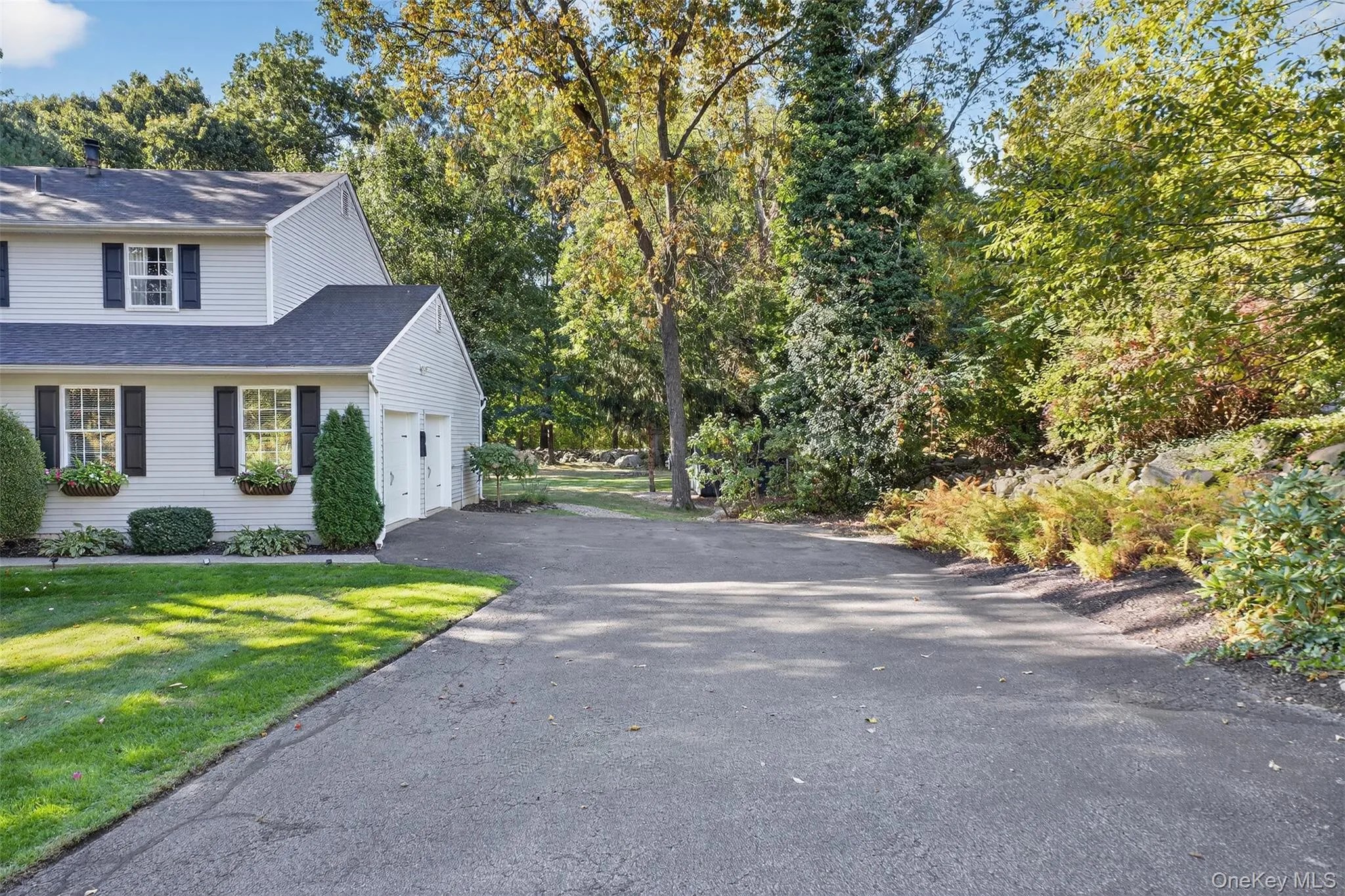 View of property exterior with a shingled roof, asphalt driveway, a yard, and view of wooded area View of property exterior with a shingled roof, asphalt driveway, a yard, and view of wooded area
