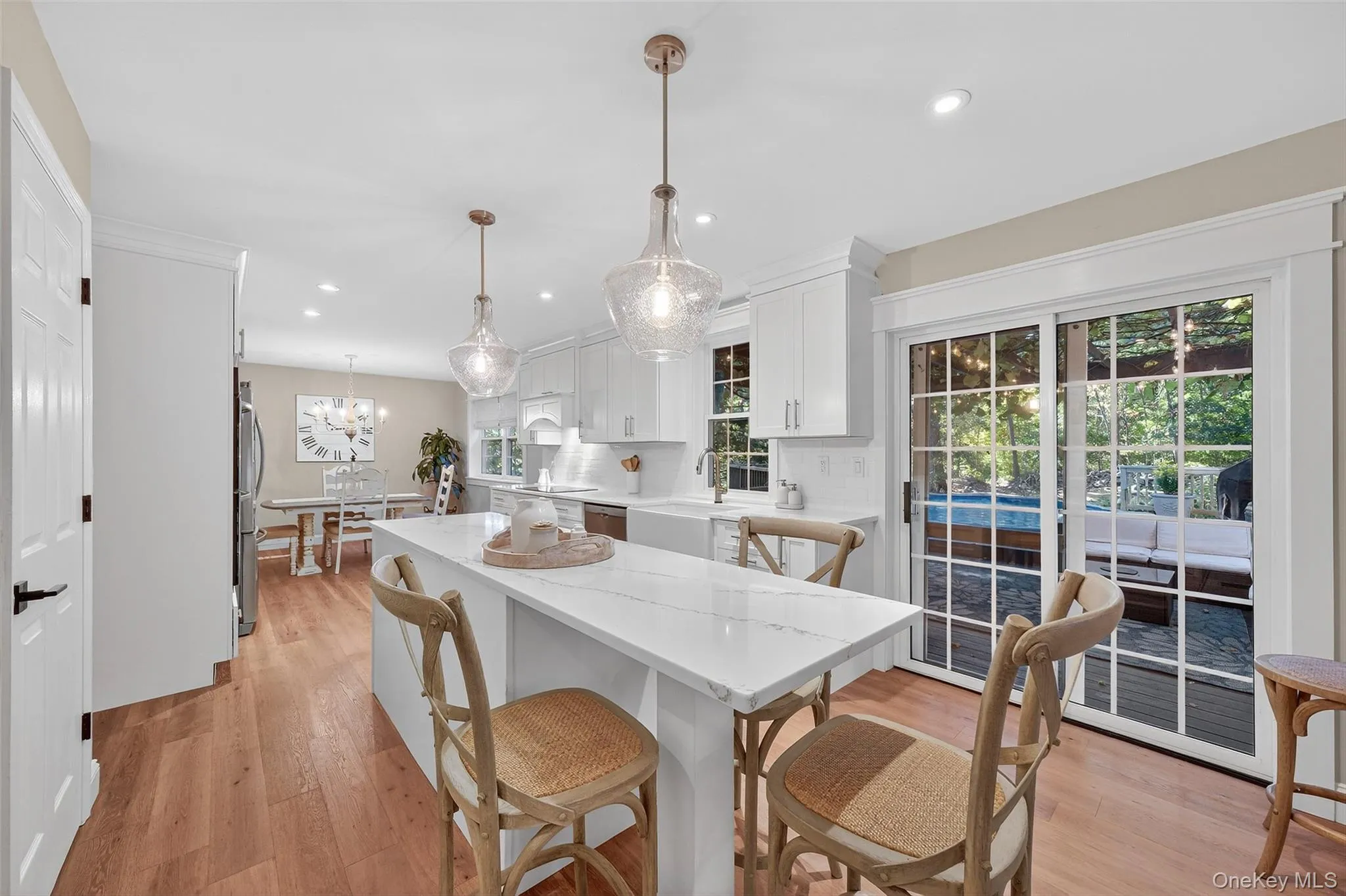 Kitchen featuring white cabinets, light wood-style floors, decorative light fixtures, light stone countertops, and a breakfast bar Kitchen featuring white cabinets, light wood-style floors, decorative light fixtures, light stone countertops, and a breakfast bar