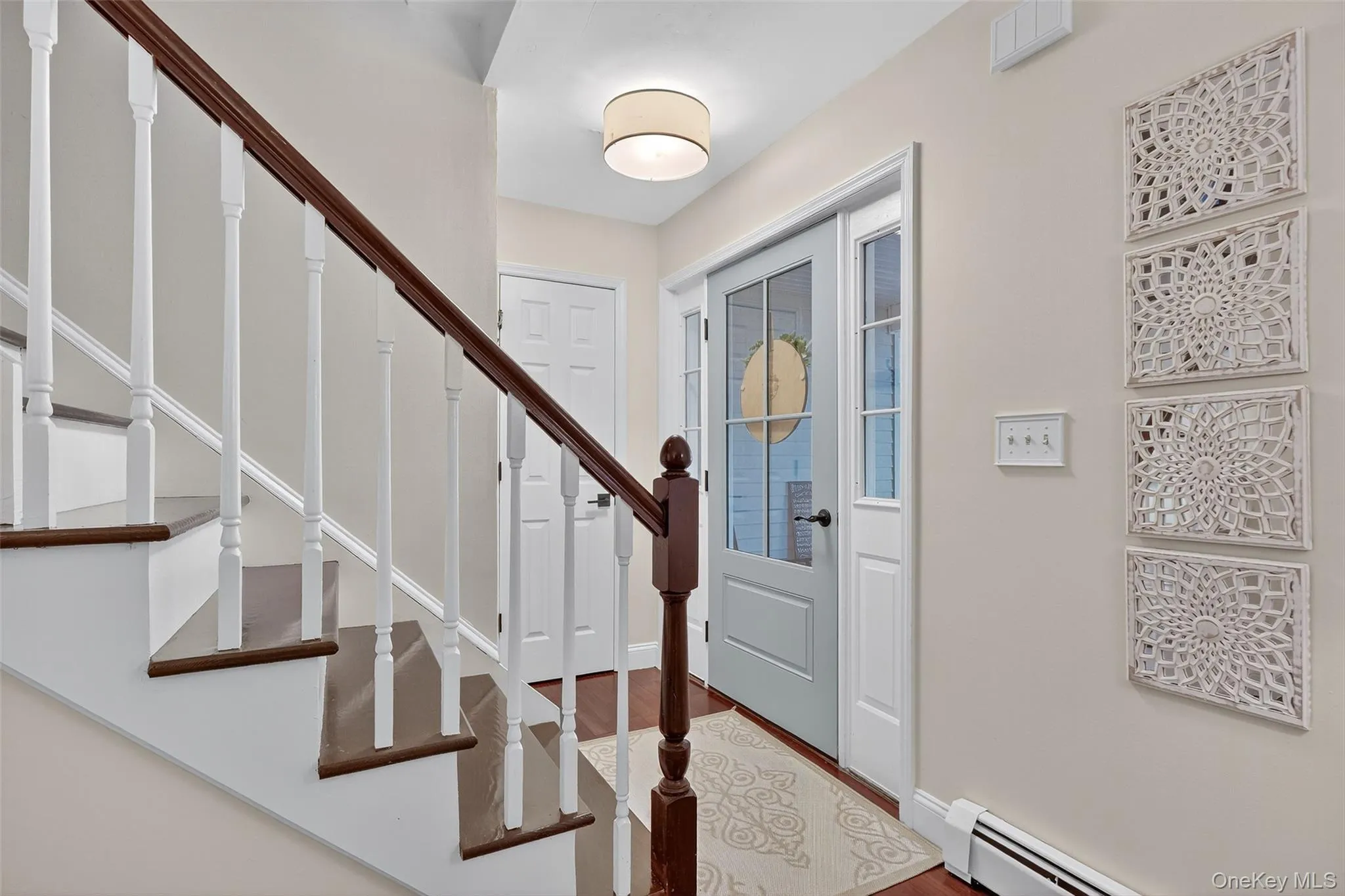 Foyer entrance with a baseboard heating unit, wood finished floors, and stairs Foyer entrance with a baseboard heating unit, wood finished floors, and stairs