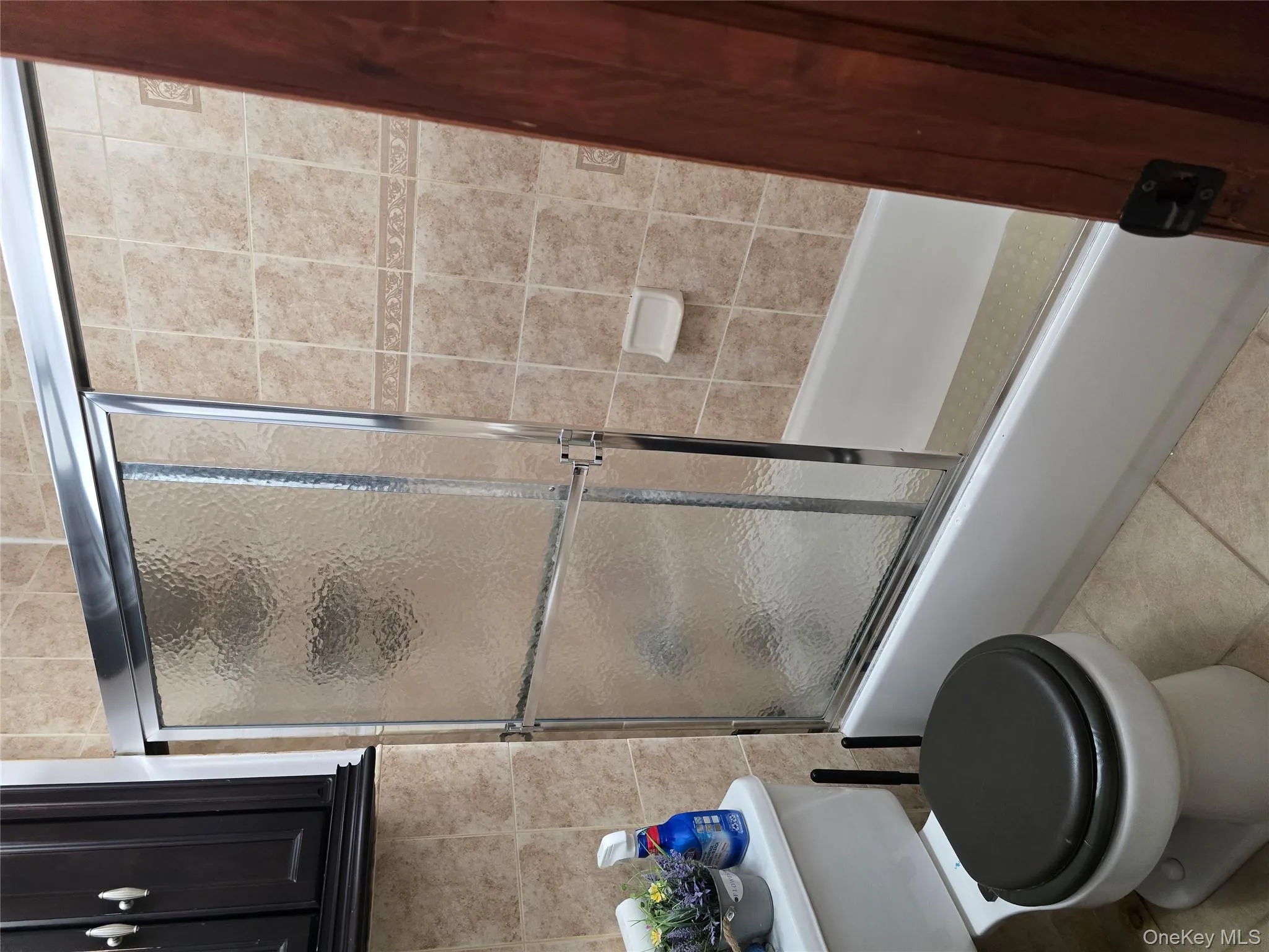 Bathroom featuring shower / bath combination with glass door, tile walls, and light tile patterned flooring Bathroom featuring shower / bath combination with glass door, tile walls, and light tile patterned flooring