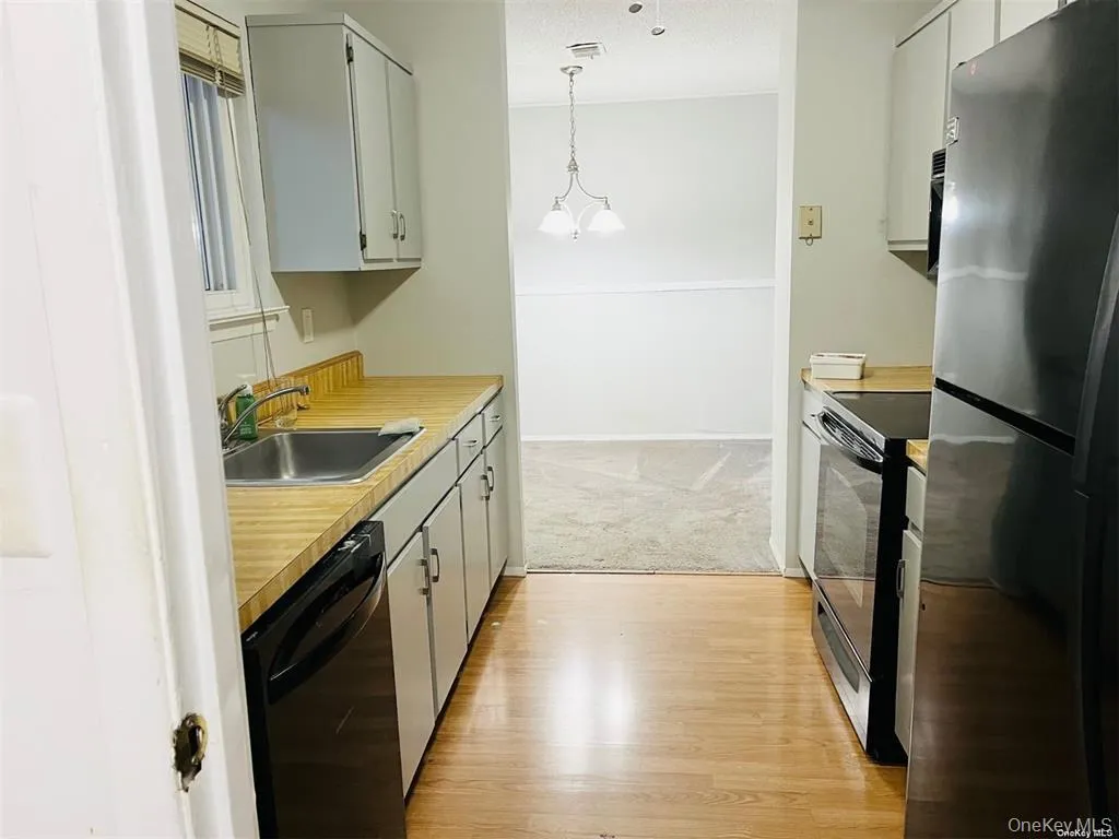 Kitchen with black appliances, light countertops, hanging light fixtures, gray cabinetry, and light wood-type flooring Kitchen with black appliances, light countertops, hanging light fixtures, gray cabinetry, and light wood-type flooring