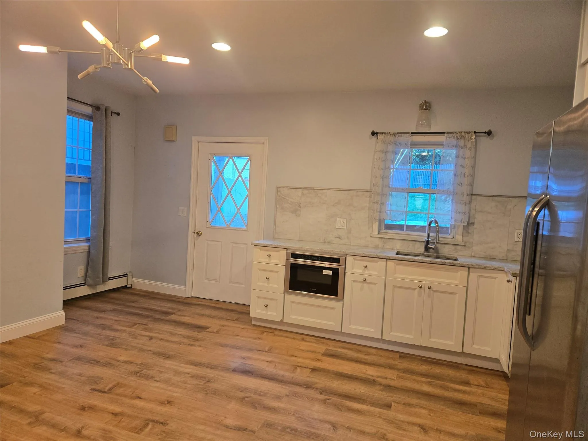 Kitchen with white cabinets, stainless steel appliances, light stone countertops, recessed lighting, and baseboard heating Kitchen with white cabinets, stainless steel appliances, light stone countertops, recessed lighting, and baseboard heating