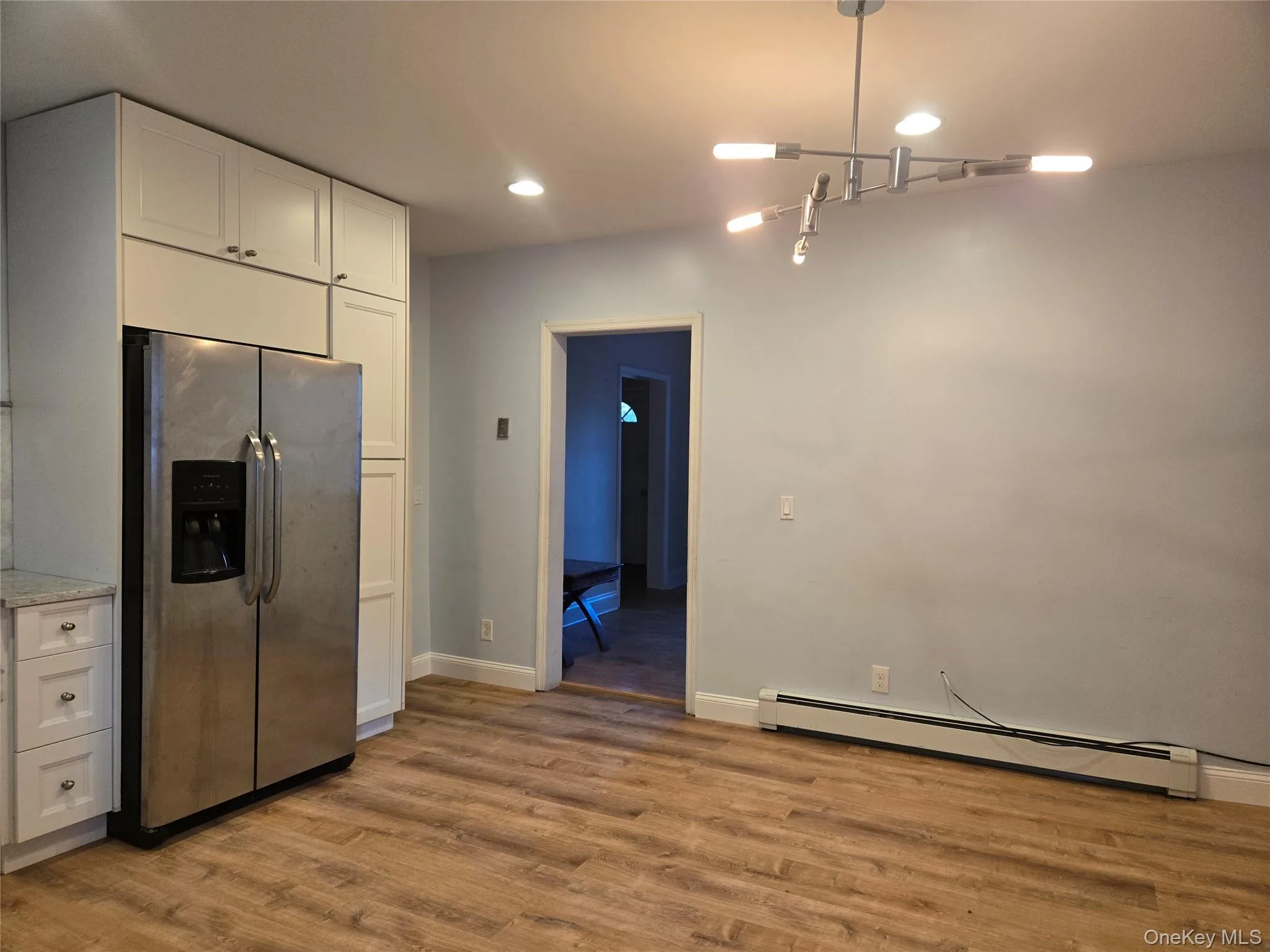 Kitchen featuring stainless steel fridge, white cabinets, a baseboard heating unit, light wood-type flooring, and recessed lighting Kitchen featuring stainless steel fridge, white cabinets, a baseboard heating unit, light wood-type flooring, and recessed lighting