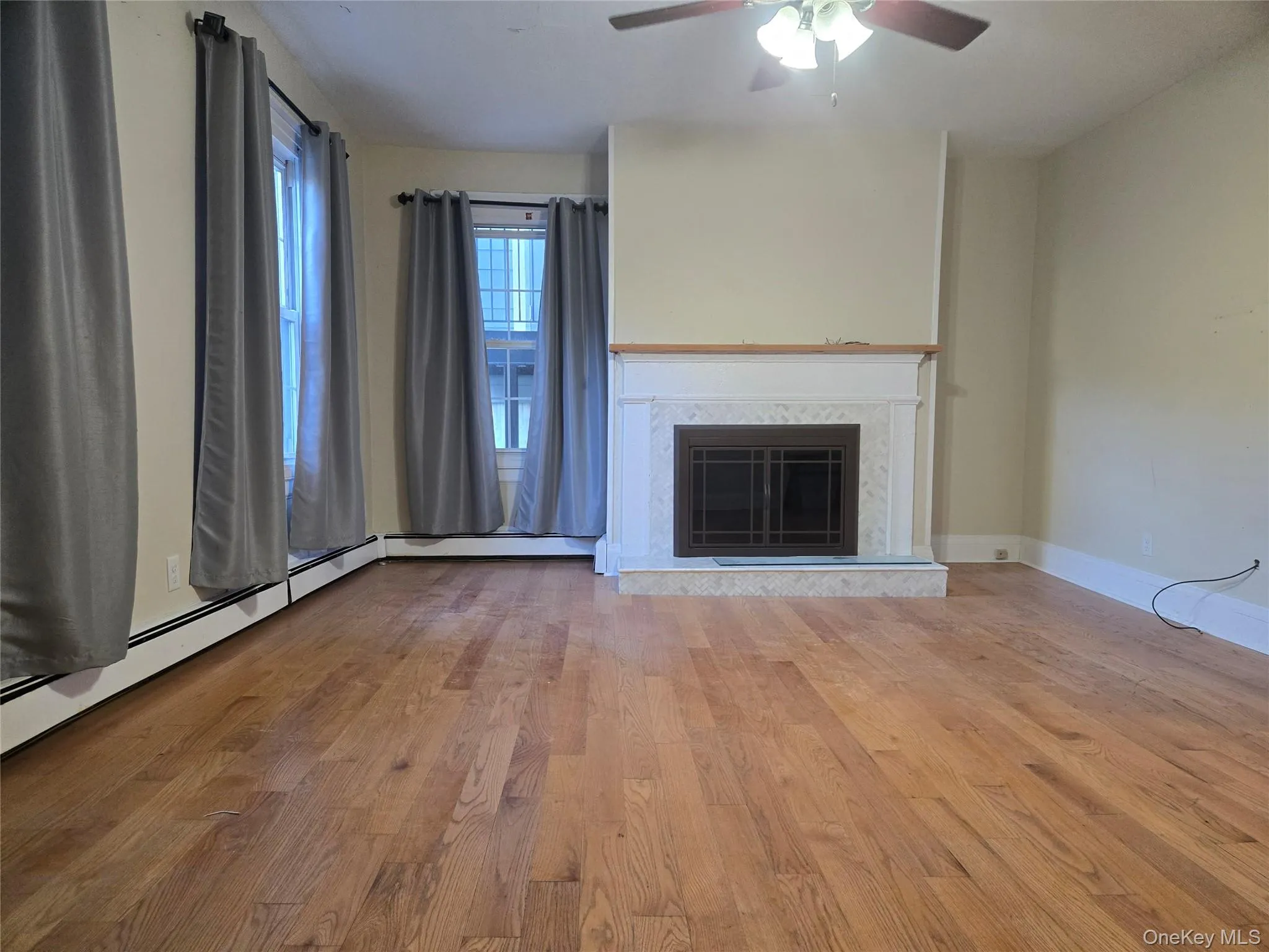 Unfurnished living room featuring a fireplace, light wood finished floors, a baseboard radiator, and ceiling fan Unfurnished living room featuring a fireplace, light wood finished floors, a baseboard radiator, and ceiling fan