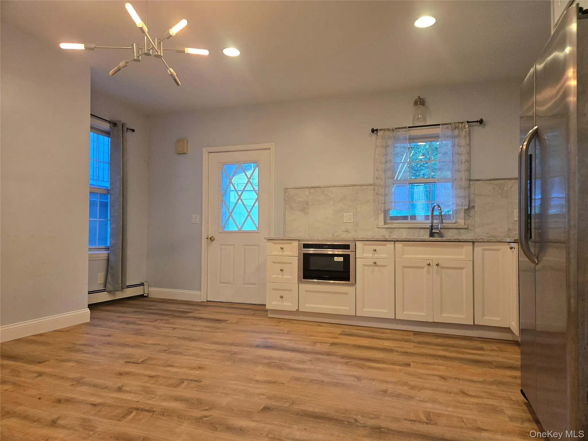 Kitchen featuring white cabinetry, appliances with stainless steel finishes, light stone countertops, light wood-style floors, and a baseboard radiator Kitchen featuring white cabinetry, appliances with stainless steel finishes, light stone countertops, light wood-style floors, and a baseboard radiator