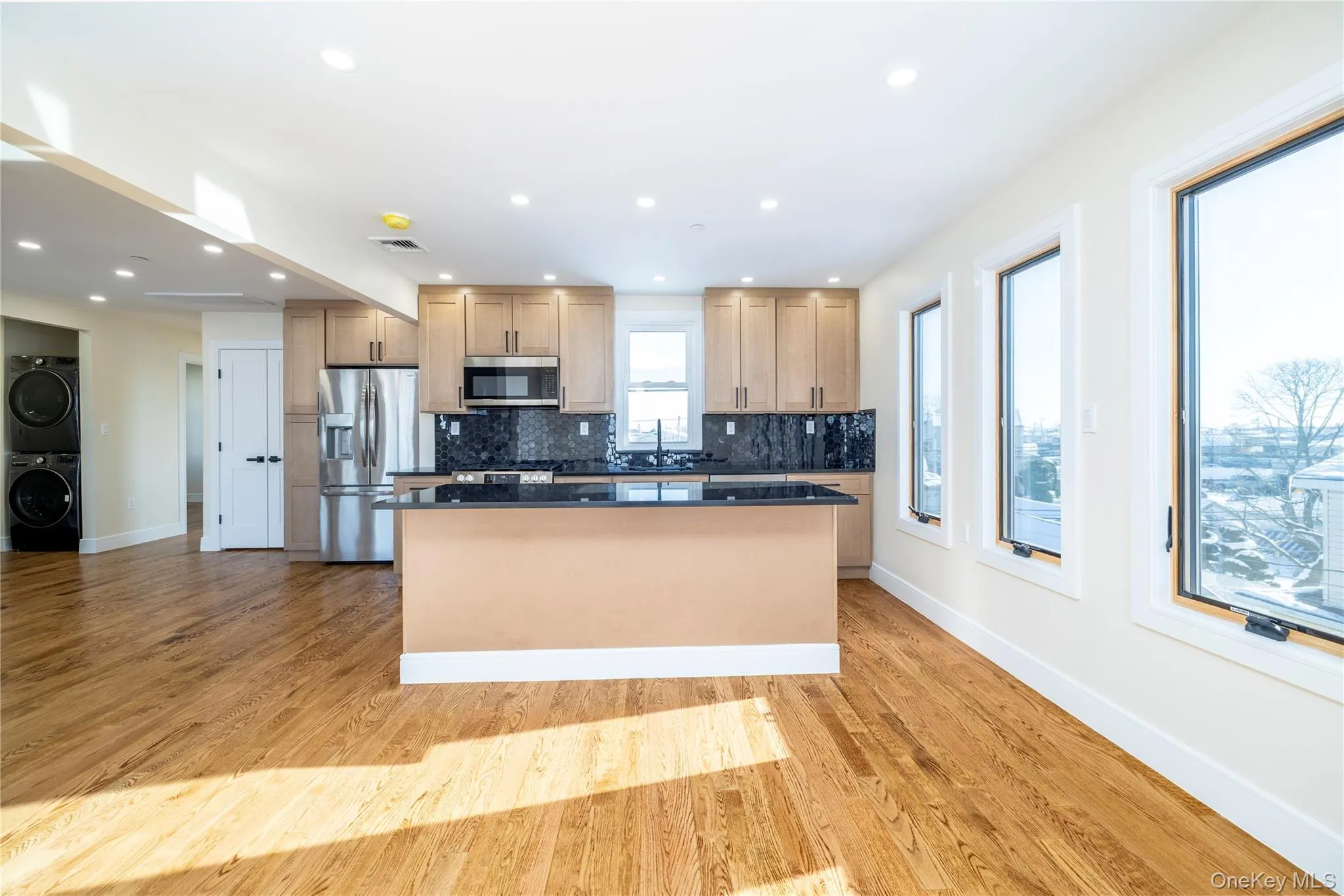 Kitchen with appliances with stainless steel finishes, stacked washer and clothes dryer, light wood-type flooring, recessed lighting, and a kitchen island Kitchen with appliances with stainless steel finishes, stacked washer and clothes dryer, light wood-type flooring, recessed lighting, and a kitchen island