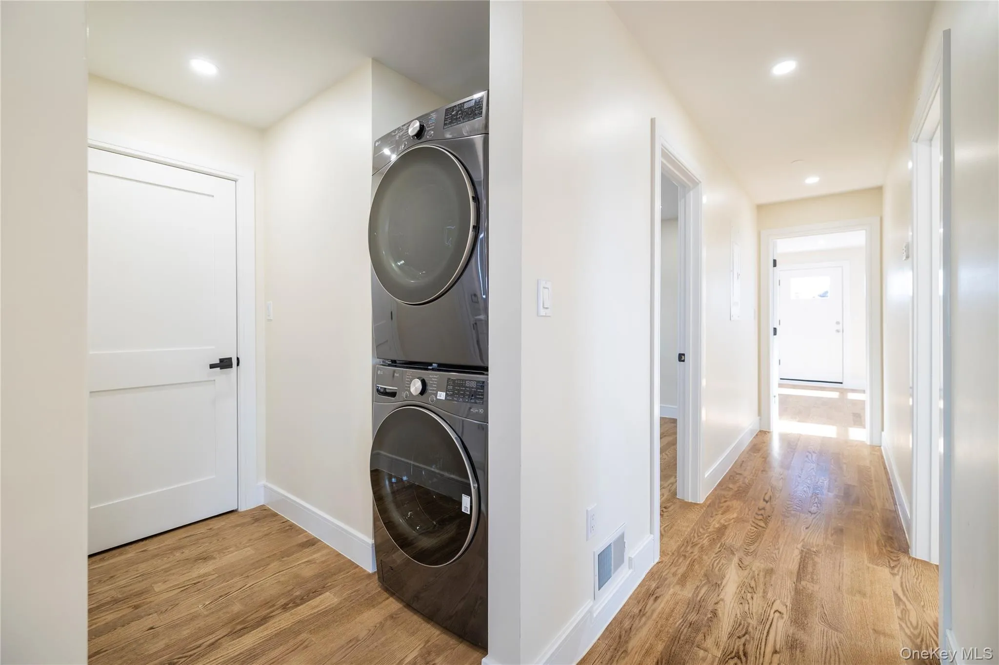 Laundry room with light wood-style floors, recessed lighting, and stacked washer and clothes dryer Laundry room with light wood-style floors, recessed lighting, and stacked washer and clothes dryer