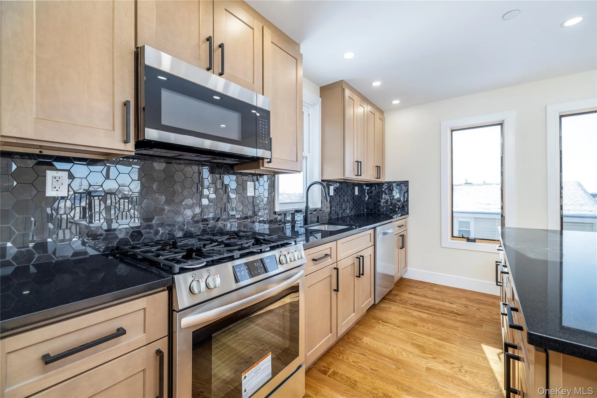 Kitchen with appliances with stainless steel finishes, dark stone countertops, backsplash, light wood-style floors, and recessed lighting Kitchen with appliances with stainless steel finishes, dark stone countertops, backsplash, light wood-style floors, and recessed lighting