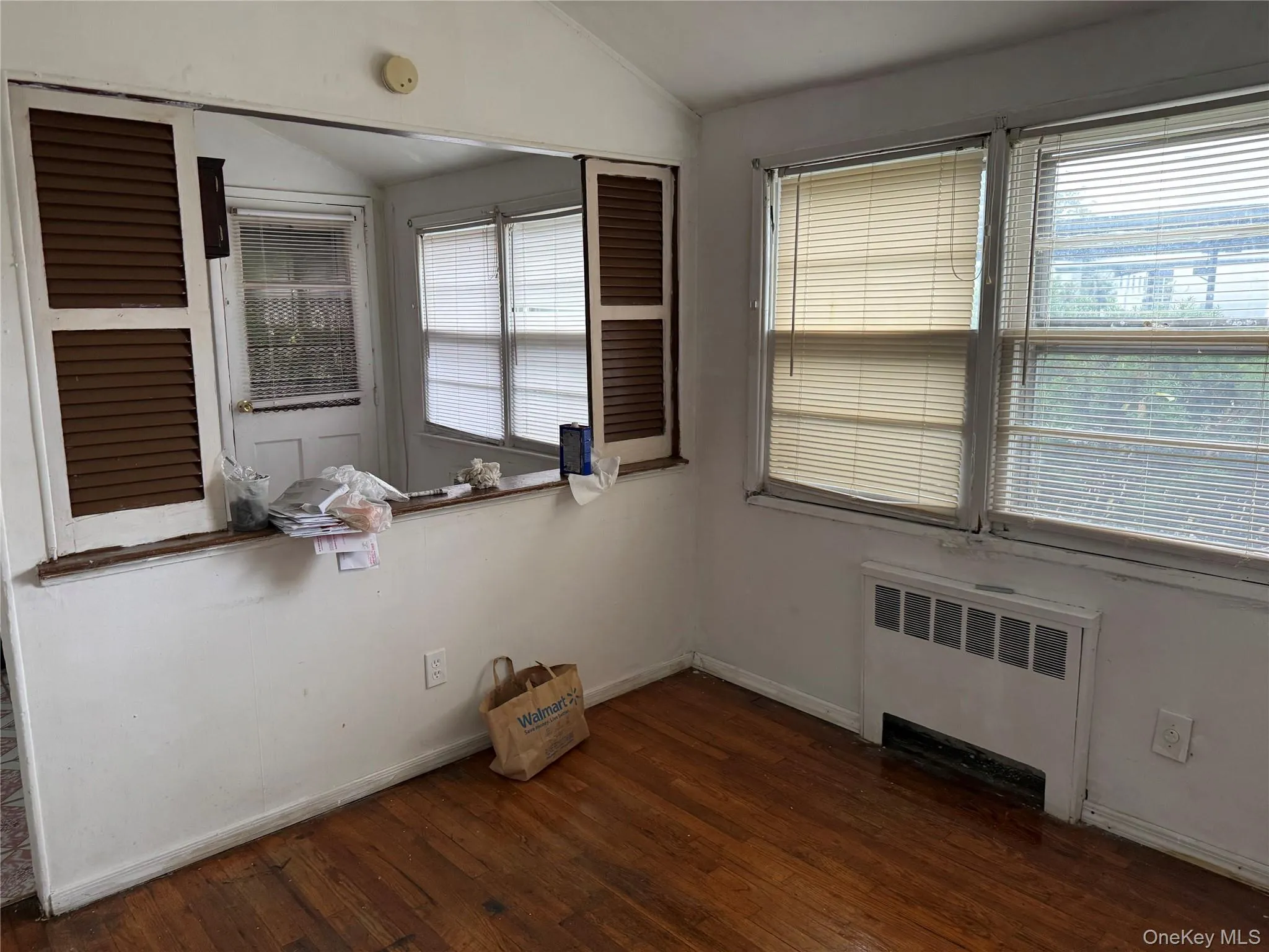 Empty room featuring lofted ceiling, radiator, and dark wood finished floors Empty room featuring lofted ceiling, radiator, and dark wood finished floors