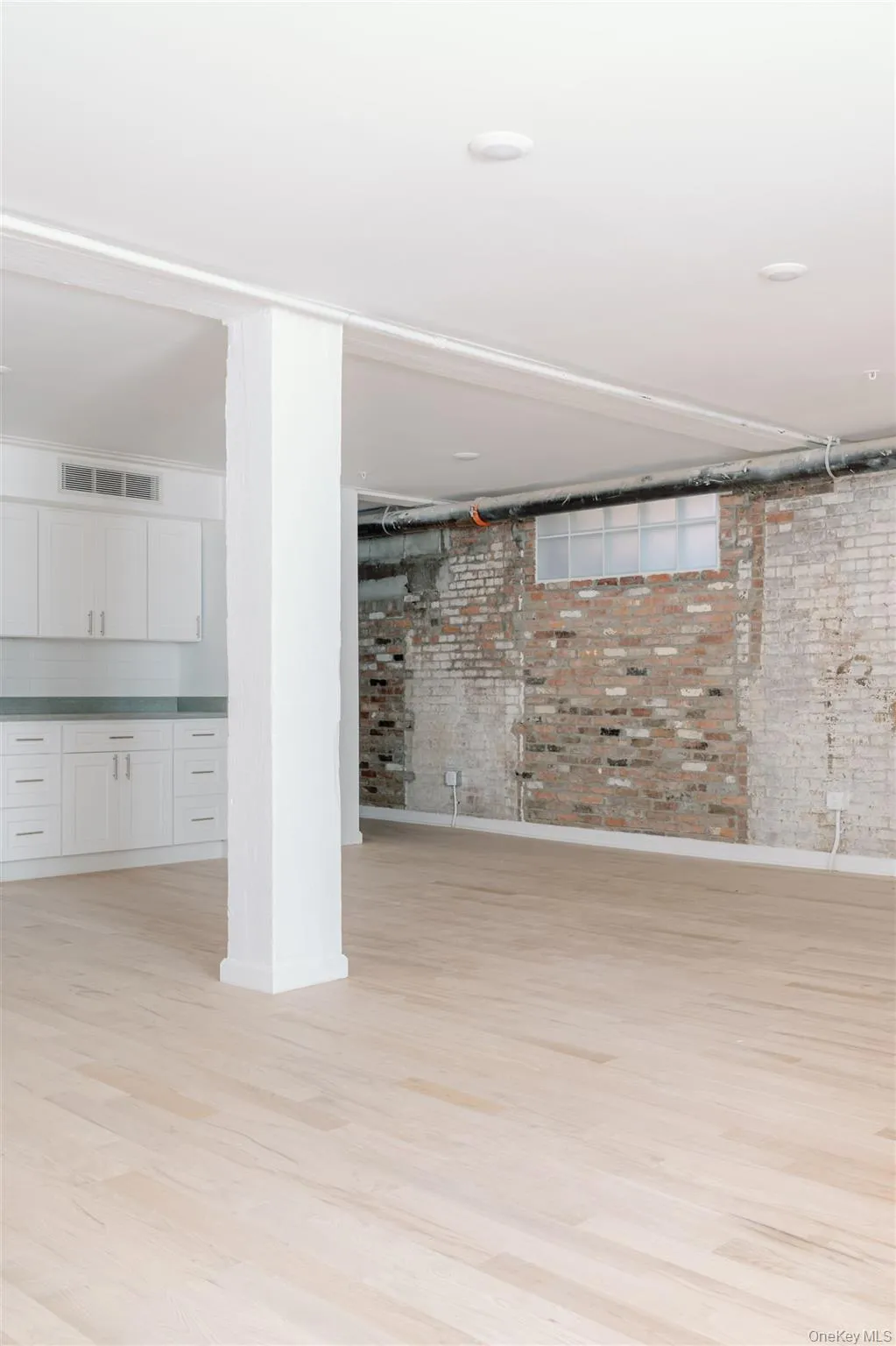 Finished basement featuring light wood-style flooring and brick wall Finished basement featuring light wood-style flooring and brick wall