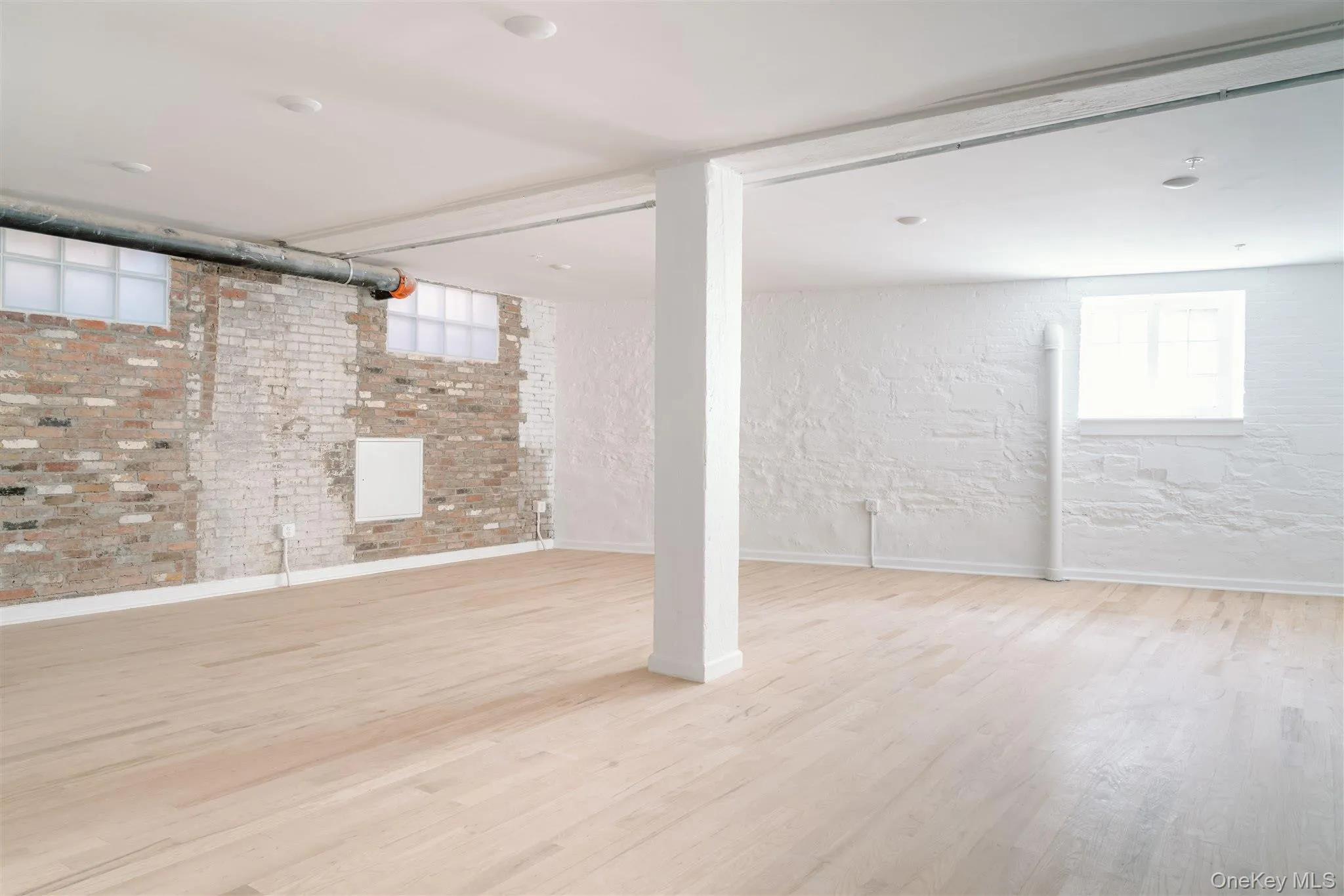 Below grade area featuring light wood-style flooring and brick wall Below grade area featuring light wood-style flooring and brick wall