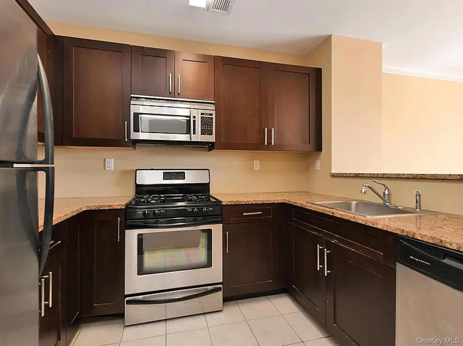 Kitchen with appliances with stainless steel finishes, light tile patterned floors, dark brown cabinetry, and ornamental molding Kitchen with appliances with stainless steel finishes, light tile patterned floors, dark brown cabinetry, and ornamental molding