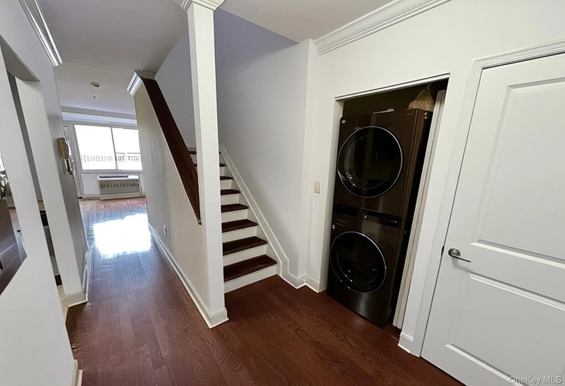 Washroom featuring stacked washing machine and dryer, crown molding, and dark wood-type flooring Washroom featuring stacked washing machine and dryer, crown molding, and dark wood-type flooring
