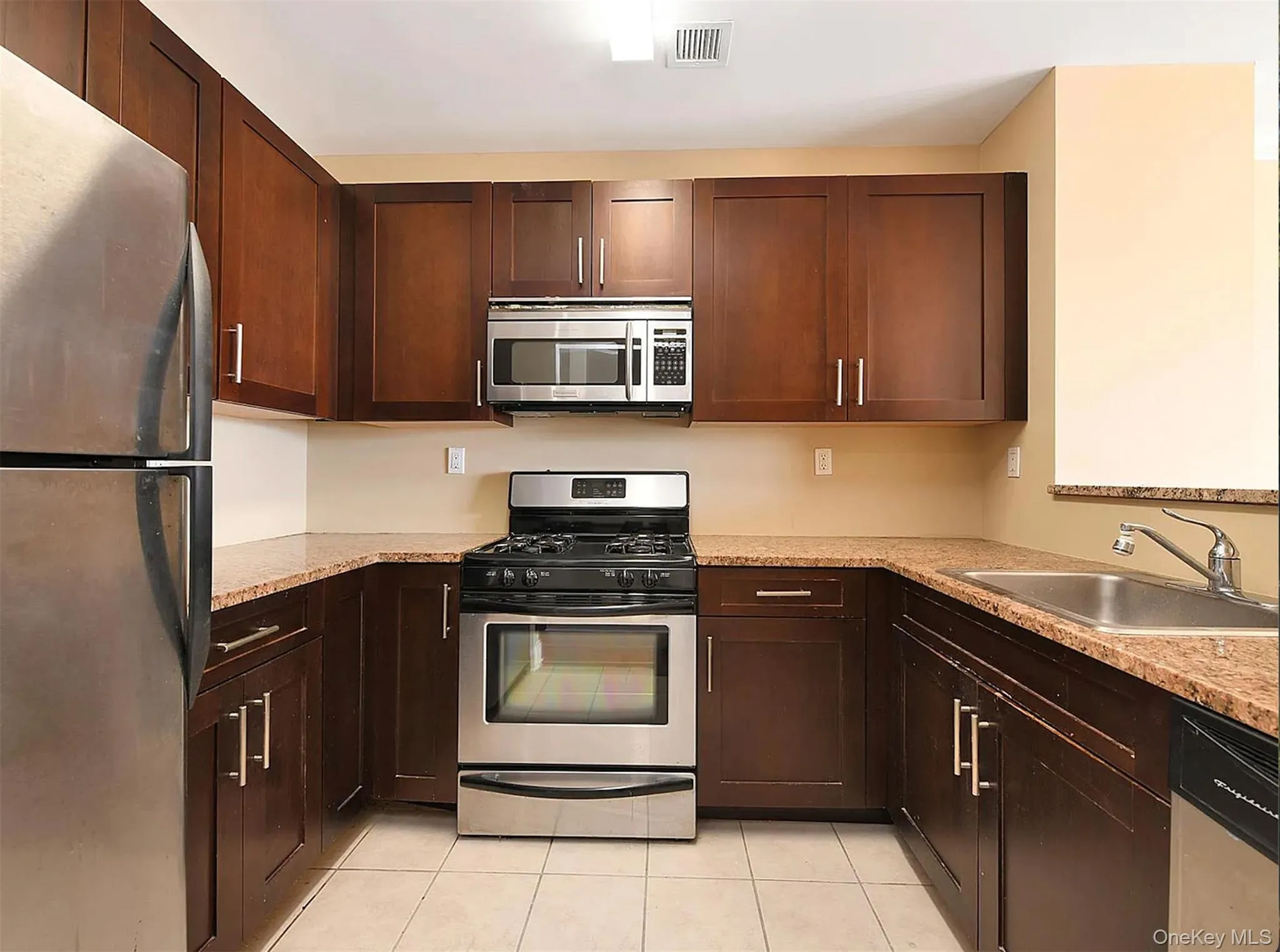 Kitchen featuring appliances with stainless steel finishes, light tile patterned floors, and dark brown cabinetry Kitchen featuring appliances with stainless steel finishes, light tile patterned floors, and dark brown cabinetry