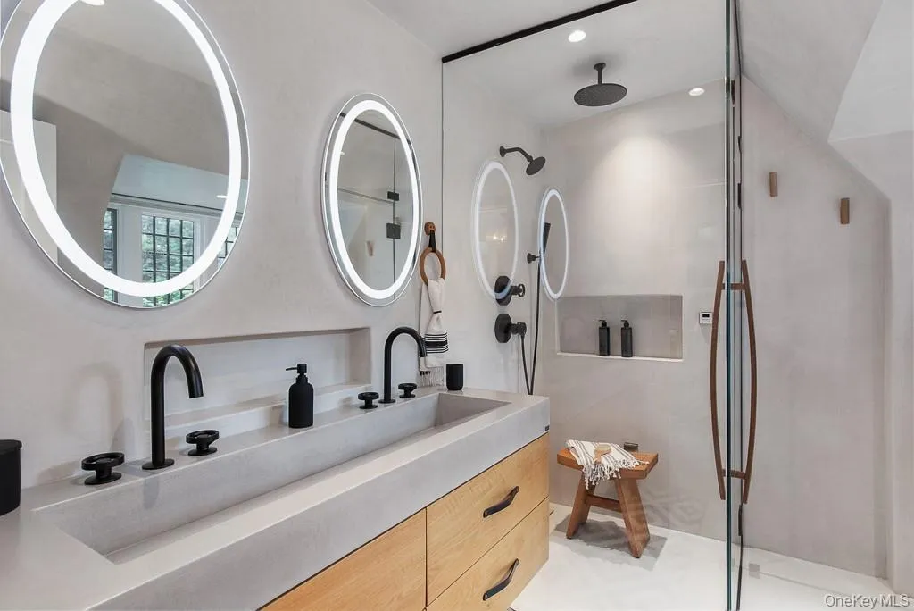 The ensuite full bathroom located off the primary bedroom's dressing area features a modern vanity with two sinks, luxurious finishes and fixtures, and an oversized shower. The ensuite full bathroom located off the primary bedroom's dressing area features a modern vanity with two sinks, luxurious finishes and fixtures, and an oversized shower.