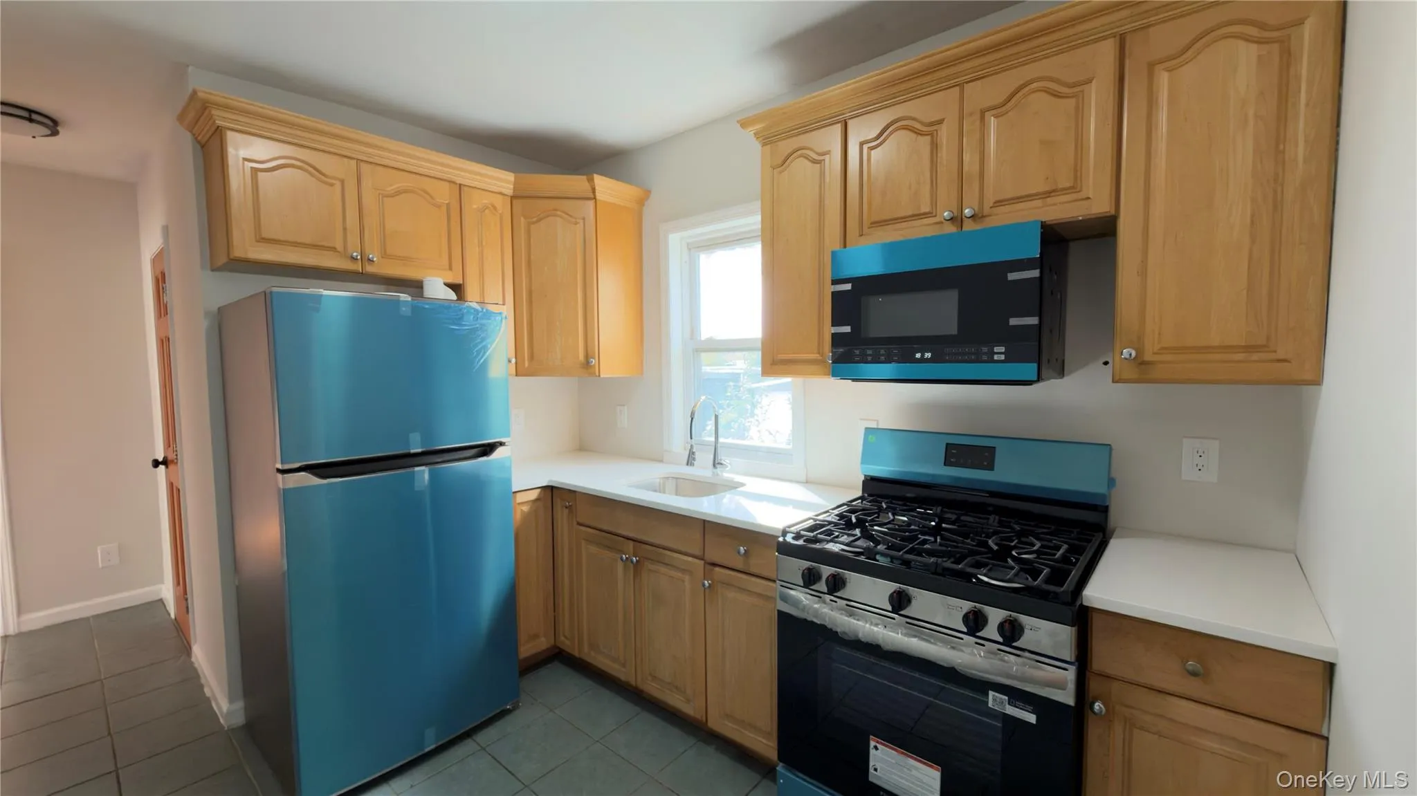 Kitchen with stainless steel appliances, dark tile patterned floors, and light brown cabinets Kitchen with stainless steel appliances, dark tile patterned floors, and light brown cabinets