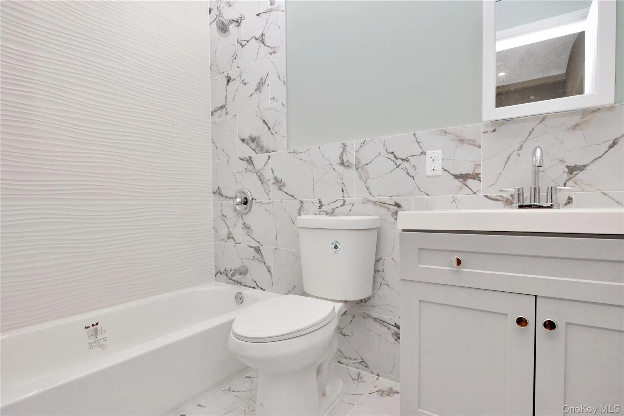 Full bathroom featuring washtub / shower combination, vanity, tile walls, and marble finish floors Full bathroom featuring washtub / shower combination, vanity, tile walls, and marble finish floors