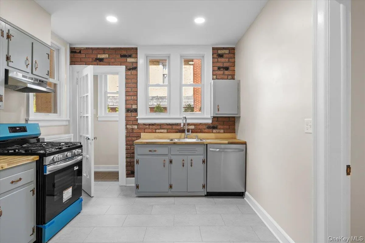 Kitchen with gray cabinetry, appliances with stainless steel finishes, under cabinet range hood, butcher block counters, and brick wall Kitchen with gray cabinetry, appliances with stainless steel finishes, under cabinet range hood, butcher block counters, and brick wall