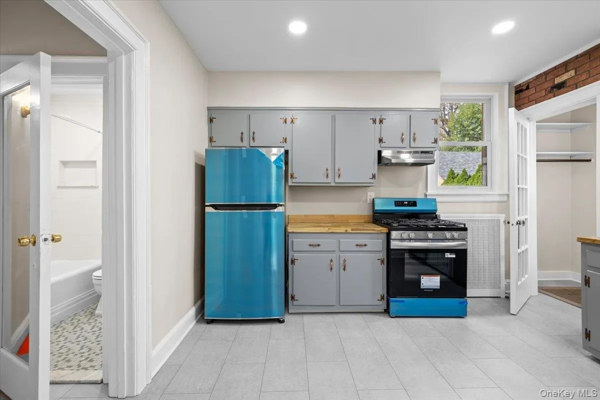 Kitchen featuring gray cabinets, freestanding refrigerator, stainless steel gas stove, light countertops, and under cabinet range hood Kitchen featuring gray cabinets, freestanding refrigerator, stainless steel gas stove, light countertops, and under cabinet range hood