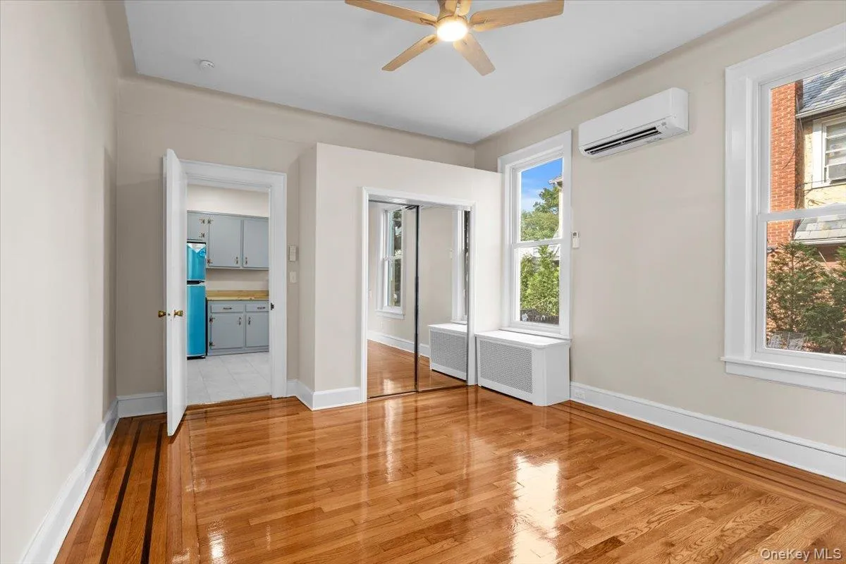 Unfurnished bedroom with light wood-style flooring, radiator heating unit, a ceiling fan, and a wall mounted AC Unfurnished bedroom with light wood-style flooring, radiator heating unit, a ceiling fan, and a wall mounted AC