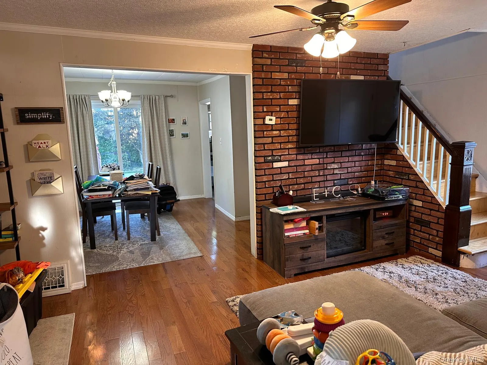 Living area with a textured ceiling, wood finished floors, ornamental molding, a ceiling fan, and stairway Living area with a textured ceiling, wood finished floors, ornamental molding, a ceiling fan, and stairway