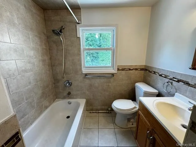 Bathroom featuring shower / washtub combination, vanity, light tile patterned floors, tile walls, and wainscoting Bathroom featuring shower / washtub combination, vanity, light tile patterned floors, tile walls, and wainscoting