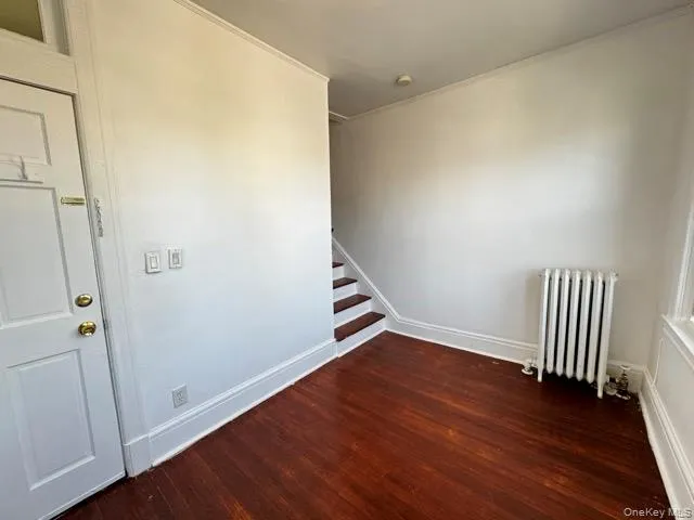 Spare room with radiator, dark wood finished floors, and stairs Spare room with radiator, dark wood finished floors, and stairs