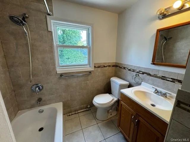 Full bath with shower / bathtub combination, vanity, light tile patterned flooring, tile walls, and wainscoting Full bath with shower / bathtub combination, vanity, light tile patterned flooring, tile walls, and wainscoting
