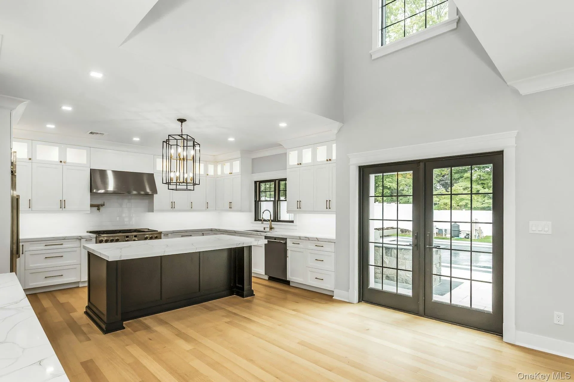 Kitchen featuring glass insert cabinets, healthy amount of natural light, a towering ceiling, french doors, and white cabinetry Kitchen featuring glass insert cabinets, healthy amount of natural light, a towering ceiling, french doors, and white cabinetry