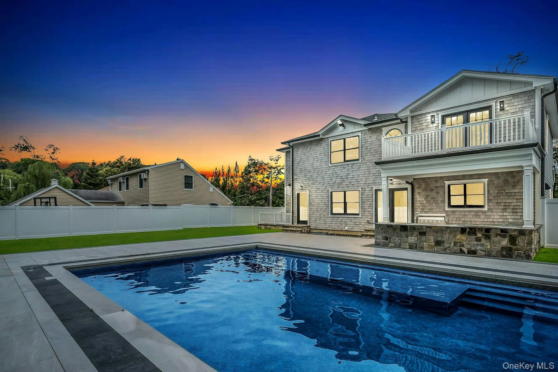 Pool at dusk featuring a patio area, a fenced backyard, and a balcony Pool at dusk featuring a patio area, a fenced backyard, and a balcony