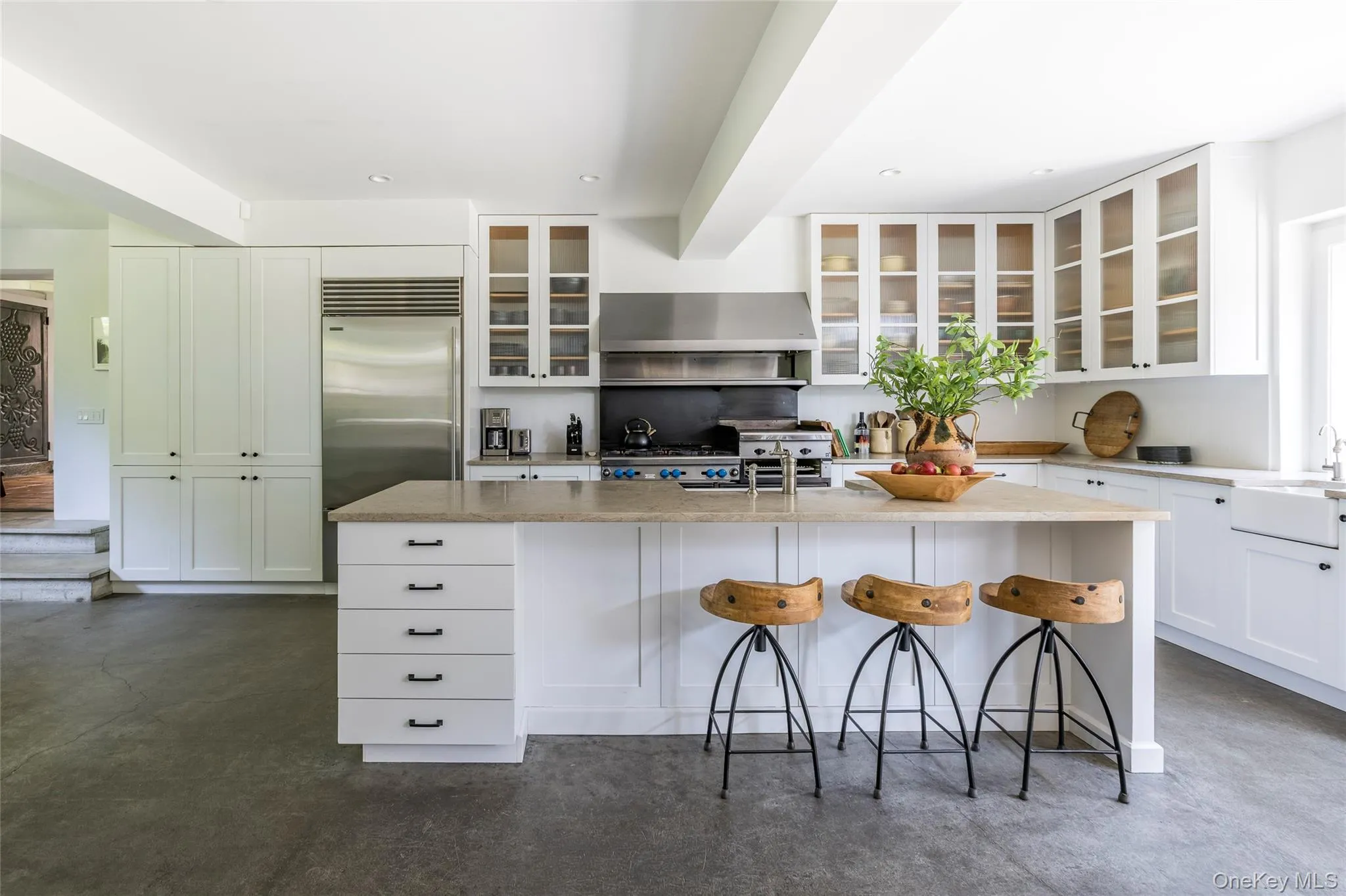 Kitchen with light stone countertops, a kitchen breakfast bar, white cabinets, finished concrete flooring, and a kitchen island with sink Kitchen with light stone countertops, a kitchen breakfast bar, white cabinets, finished concrete flooring, and a kitchen island with sink