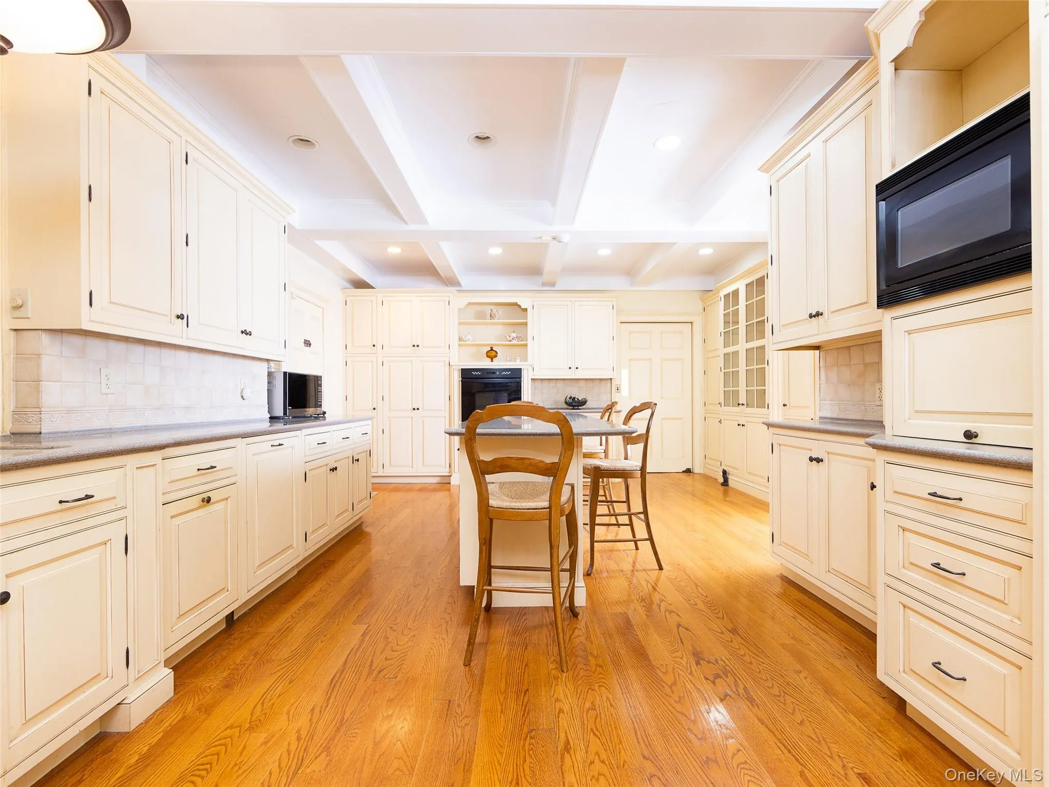 Kitchen with backsplash, open shelves, beamed ceiling, a kitchen bar, and black appliances Kitchen with backsplash, open shelves, beamed ceiling, a kitchen bar, and black appliances