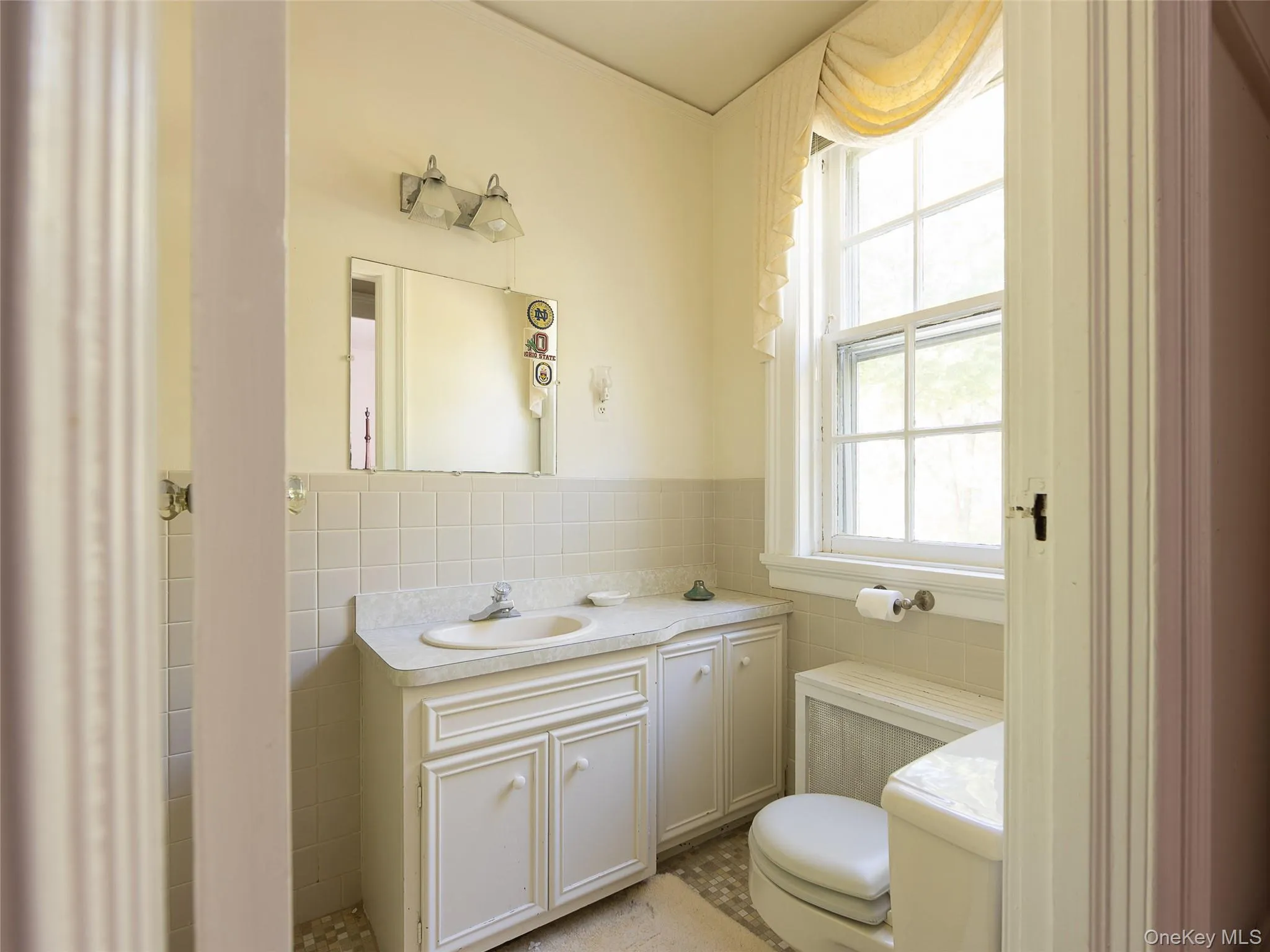 Half bath featuring tile walls, healthy amount of natural light, vanity, radiator heating unit, and wainscoting Half bath featuring tile walls, healthy amount of natural light, vanity, radiator heating unit, and wainscoting