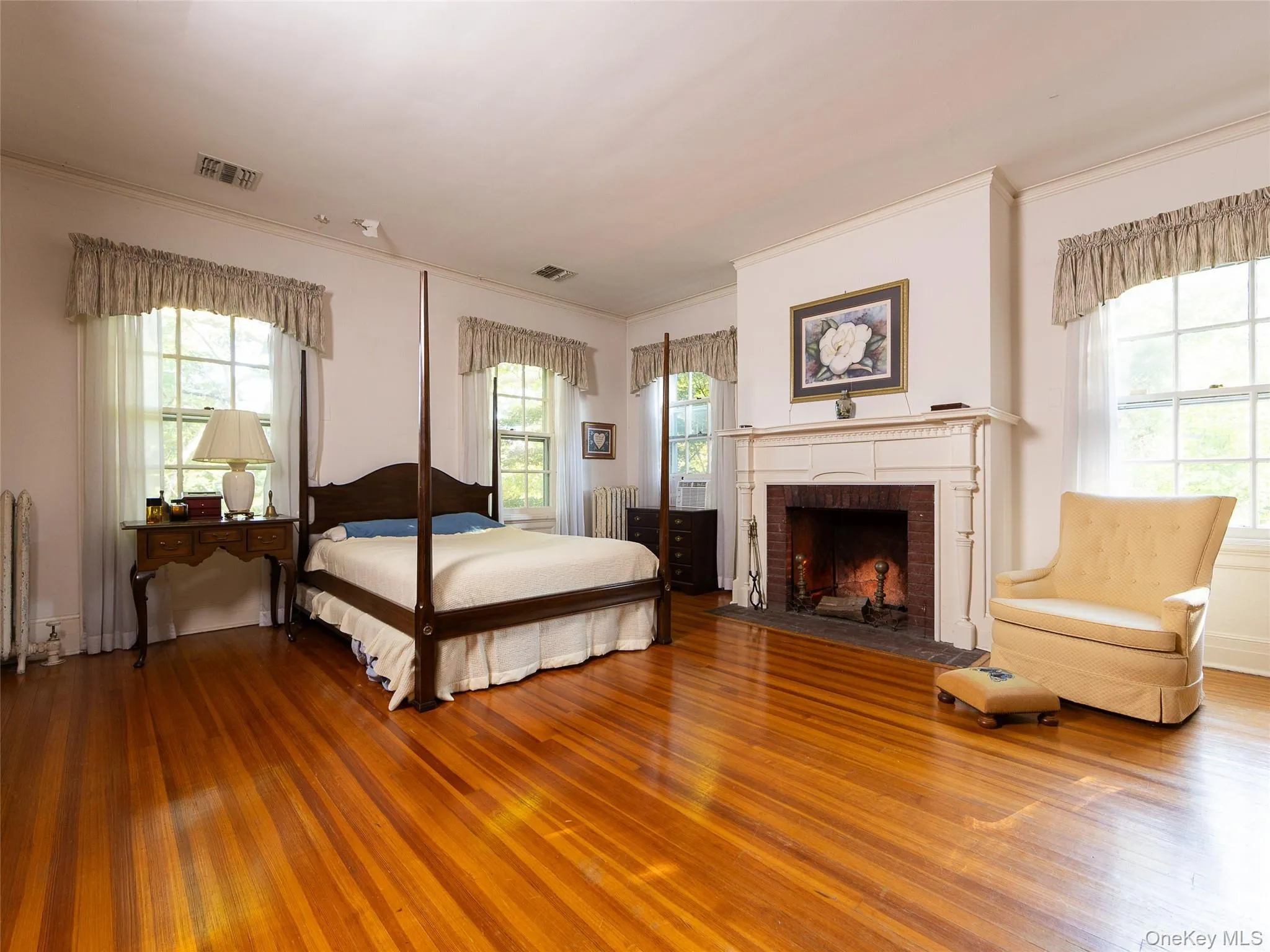 Bedroom featuring crown molding, multiple windows, wood finished floors, and a brick fireplace Bedroom featuring crown molding, multiple windows, wood finished floors, and a brick fireplace