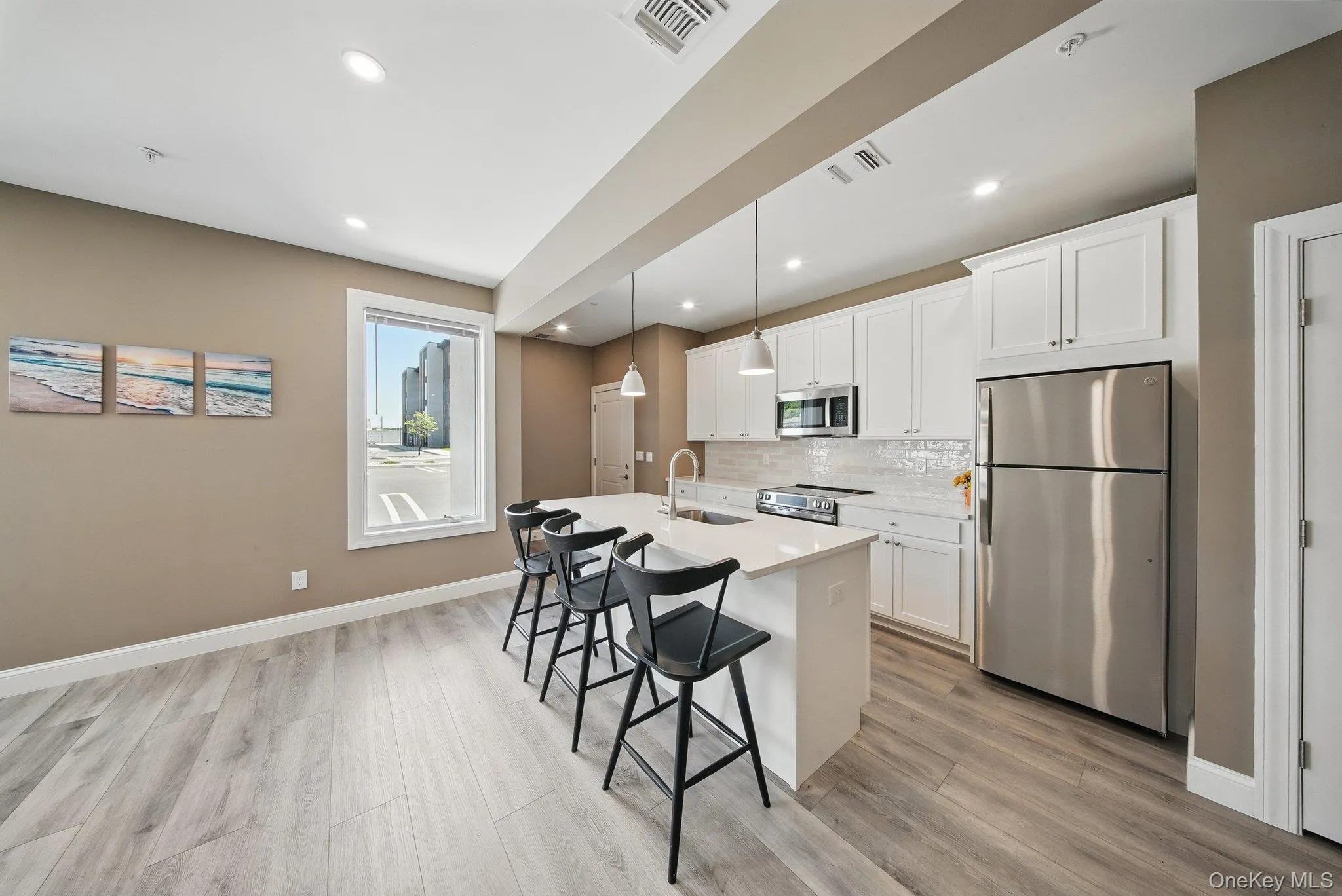 Kitchen featuring stainless steel appliances, pendant lighting, white cabinets, a center island with sink, and backsplash Kitchen featuring stainless steel appliances, pendant lighting, white cabinets, a center island with sink, and backsplash