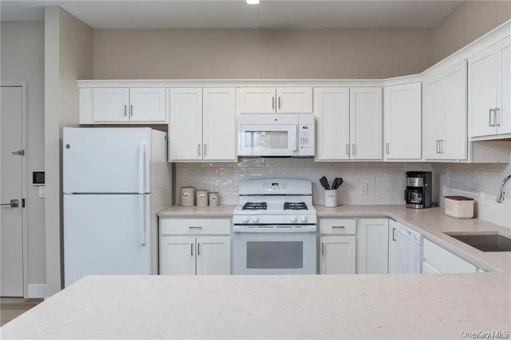 Kitchen featuring white appliances, white cabinets, light stone counters, and decorative backsplash Kitchen featuring white appliances, white cabinets, light stone counters, and decorative backsplash