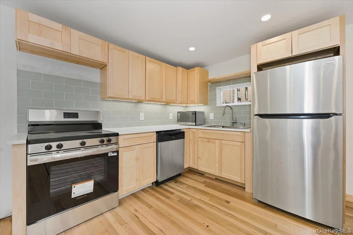 Kitchen featuring light brown cabinetry, appliances with stainless steel finishes, light countertops, decorative backsplash, and light wood finished floors Kitchen featuring light brown cabinetry, appliances with stainless steel finishes, light countertops, decorative backsplash, and light wood finished floors