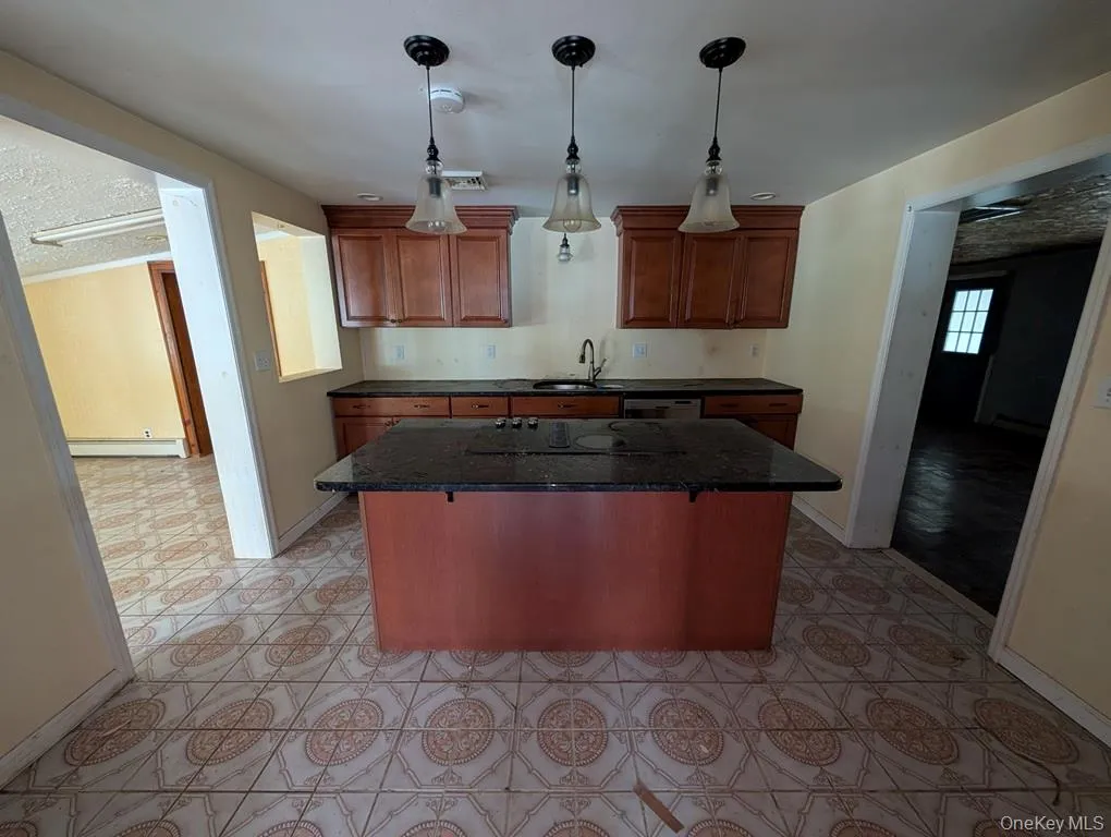 Kitchen featuring a center island, dark stone countertops, decorative light fixtures, brown cabinets, and a textured ceiling Kitchen featuring a center island, dark stone countertops, decorative light fixtures, brown cabinets, and a textured ceiling