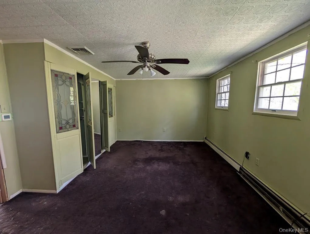 Unfurnished room with baseboard heating, ornamental molding, dark carpet, and ceiling fan Unfurnished room with baseboard heating, ornamental molding, dark carpet, and ceiling fan