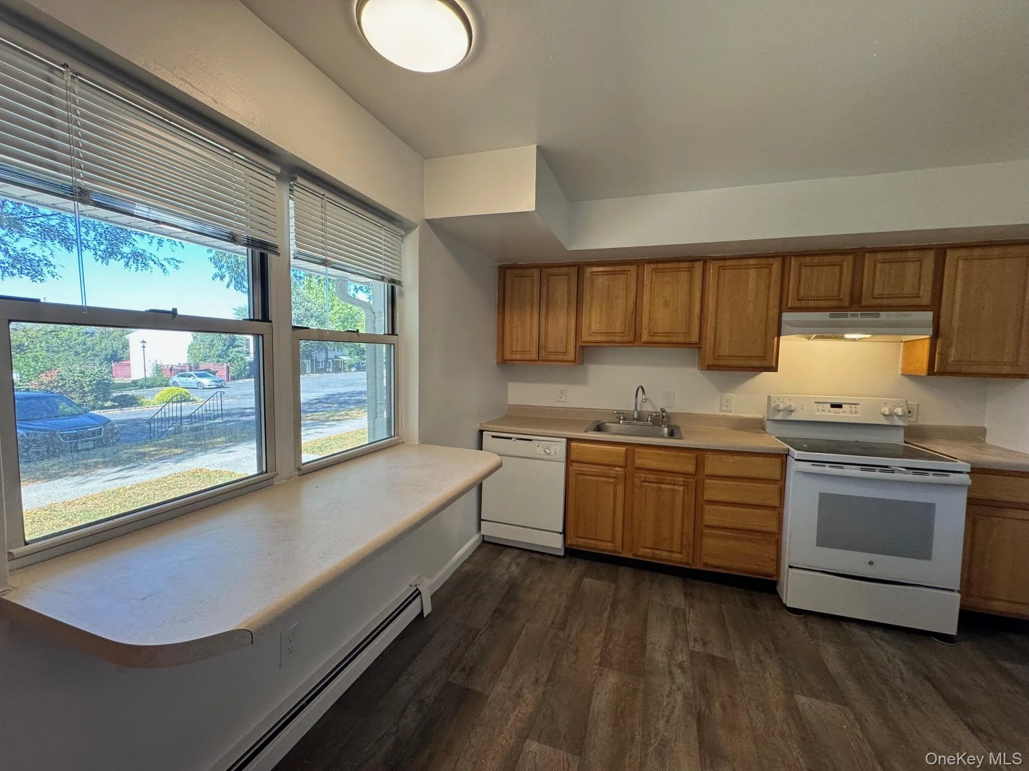Kitchen featuring a baseboard heating unit, white appliances, light countertops, dark wood-type flooring, and under cabinet range hood Kitchen featuring a baseboard heating unit, white appliances, light countertops, dark wood-type flooring, and under cabinet range hood